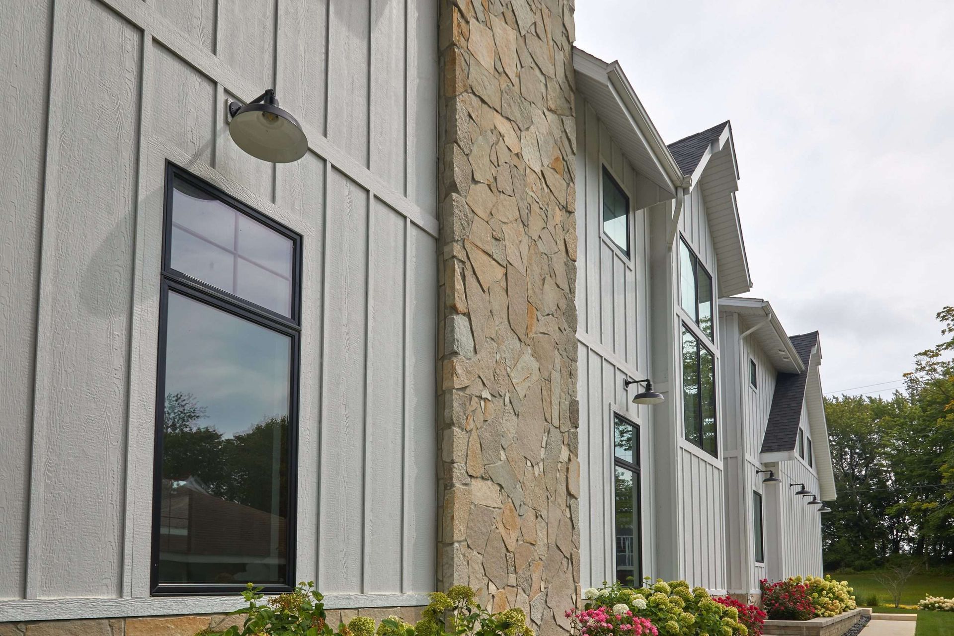 Exterior of a modern building with stone and white siding, tall windows, and flower beds along the wall