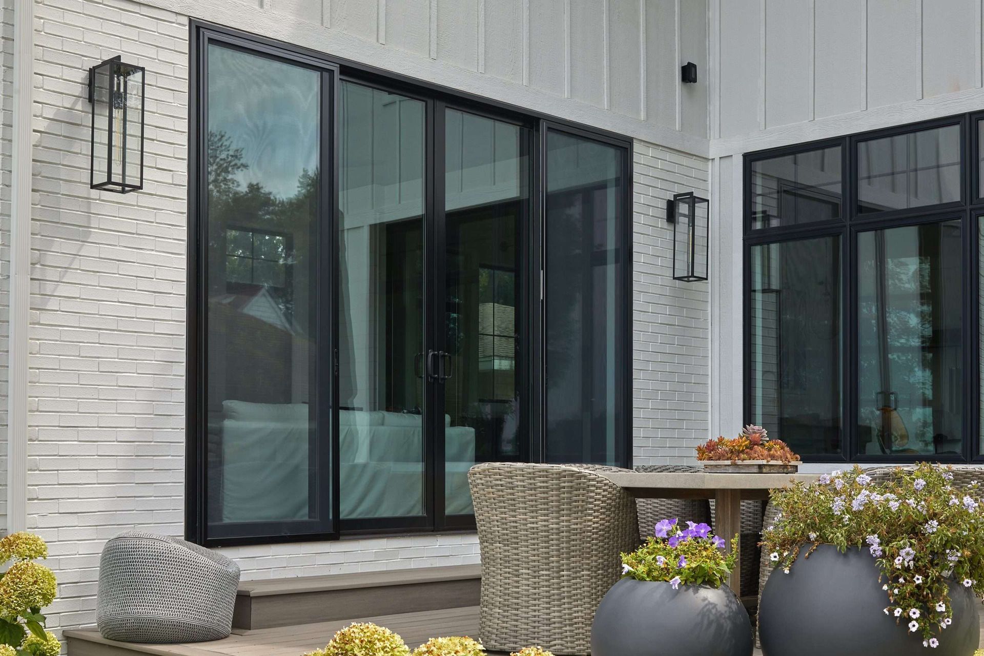 Modern patio with black-framed glass doors, white brick wall, and potted flowers and decor.