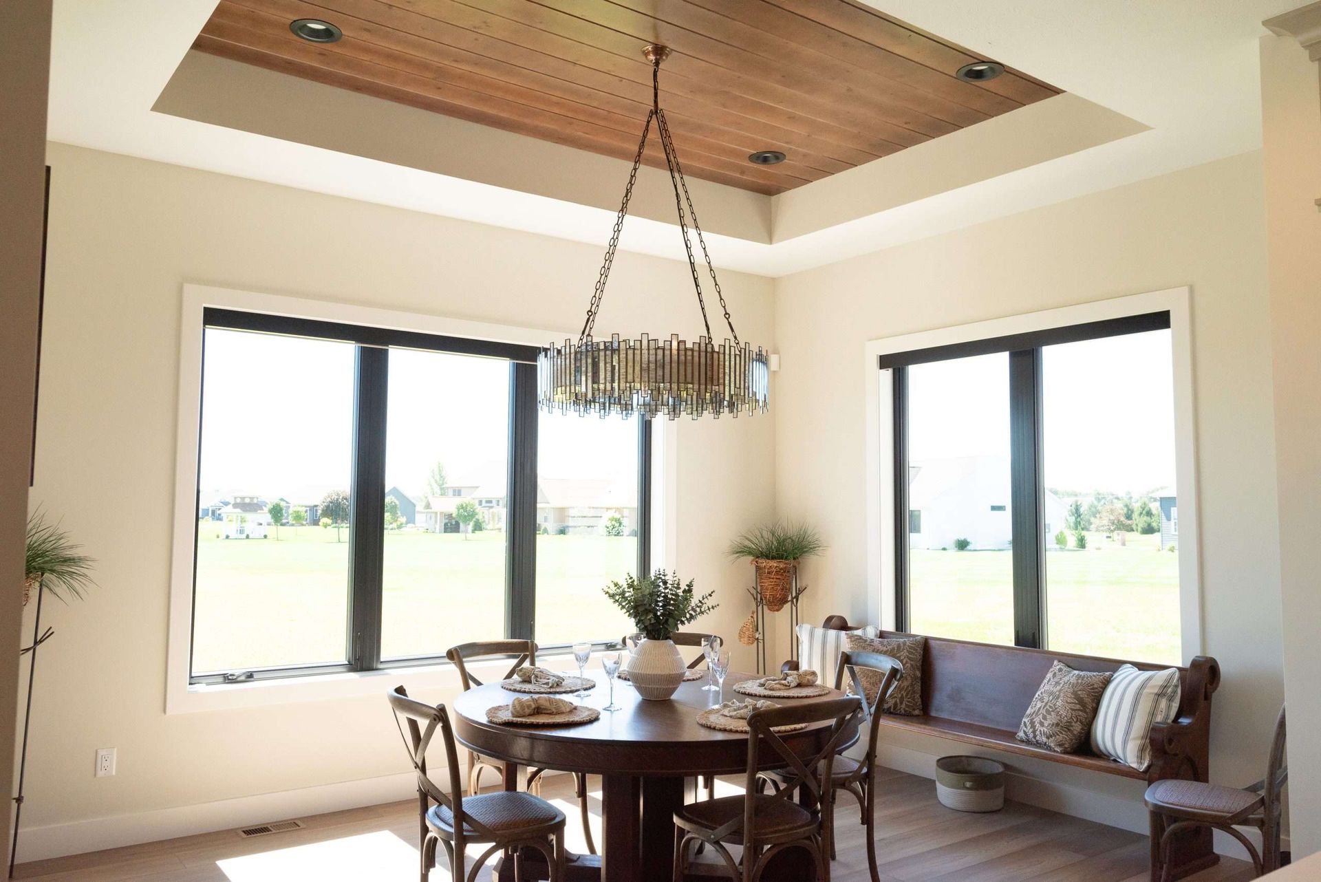 Bright dining nook with a round table, chandelier, large windows, and a cushioned bench seating area