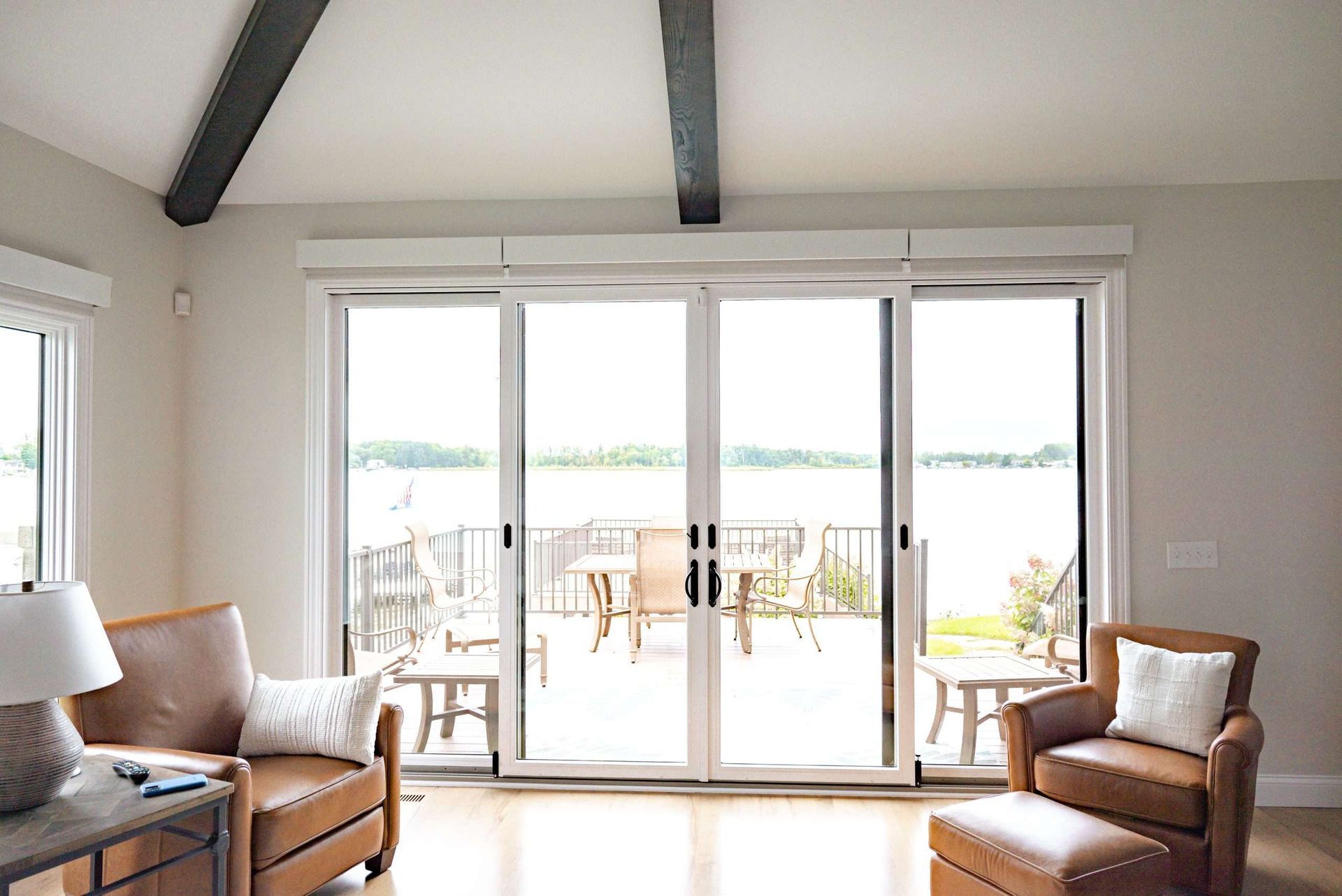 Bright living room with tan chairs and a large sliding glass door opening to a waterfront patio.