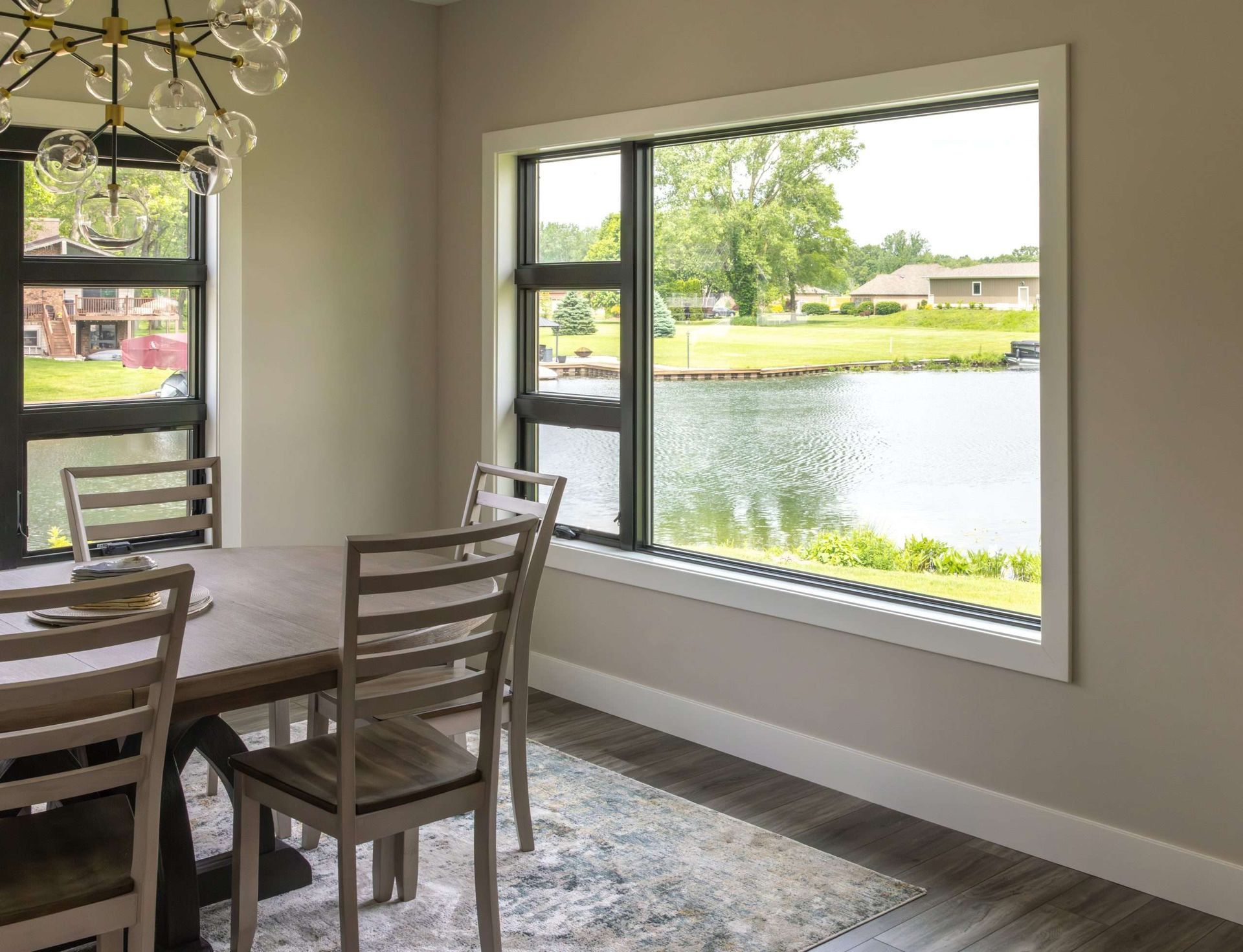 Dining room with a table and chairs beside a large window overlooking a lake and green lawn