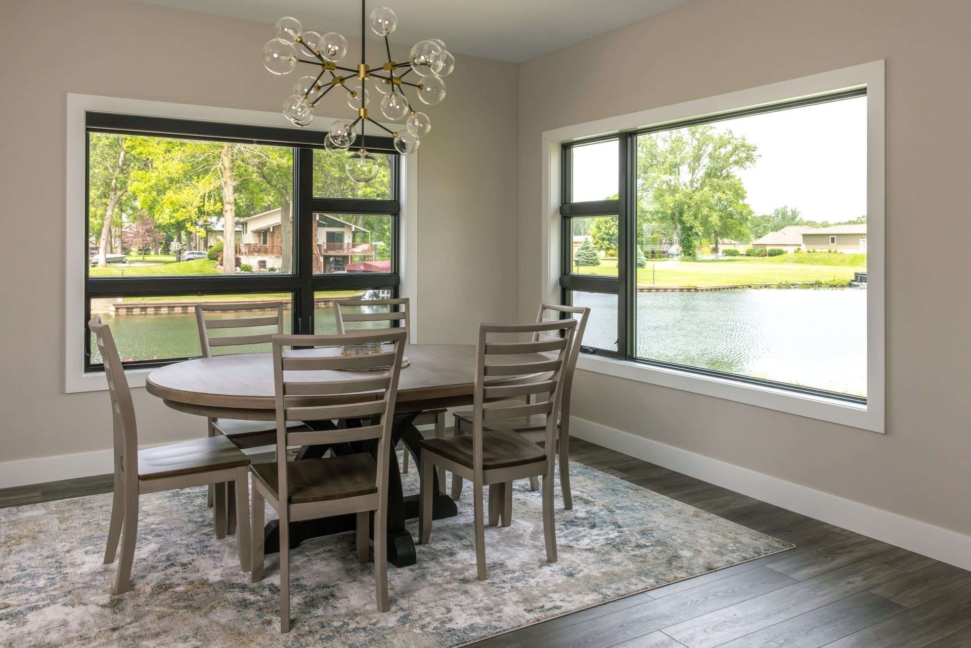 Dining room with round table and chairs by large windows overlooking a green lake view