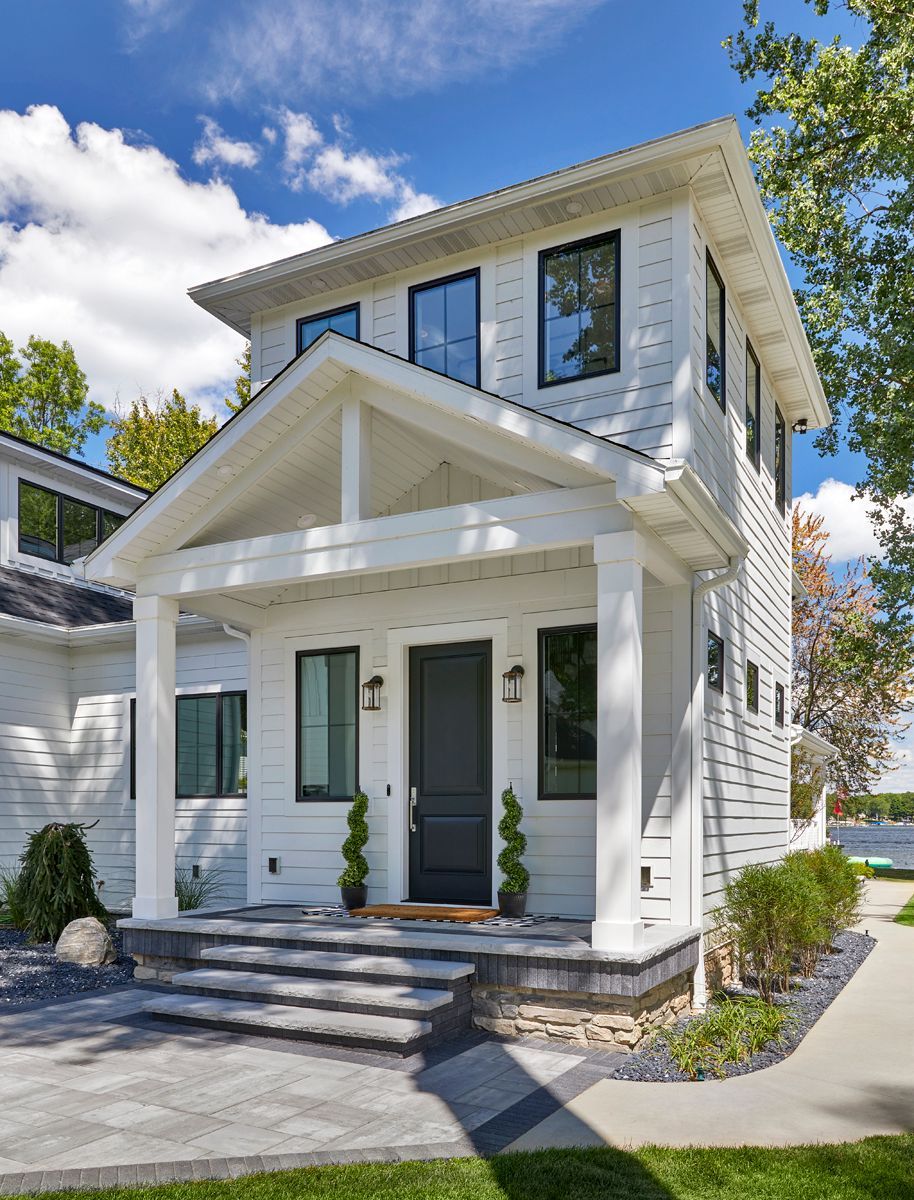 Two-story white house with front porch, blue-trimmed windows, and a small front yard under a bright sky