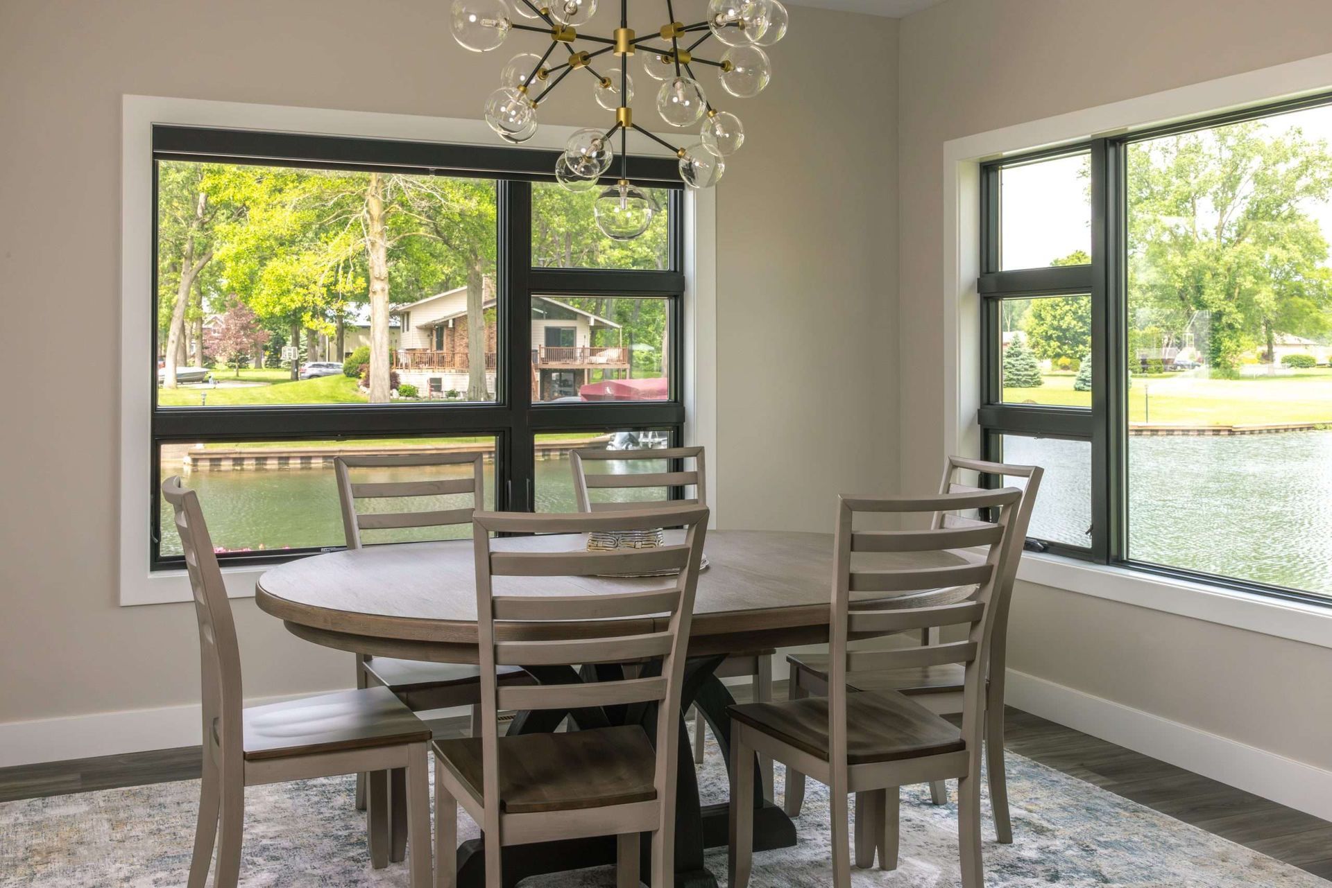 Dining area with round table and chairs by large windows overlooking a green lawn