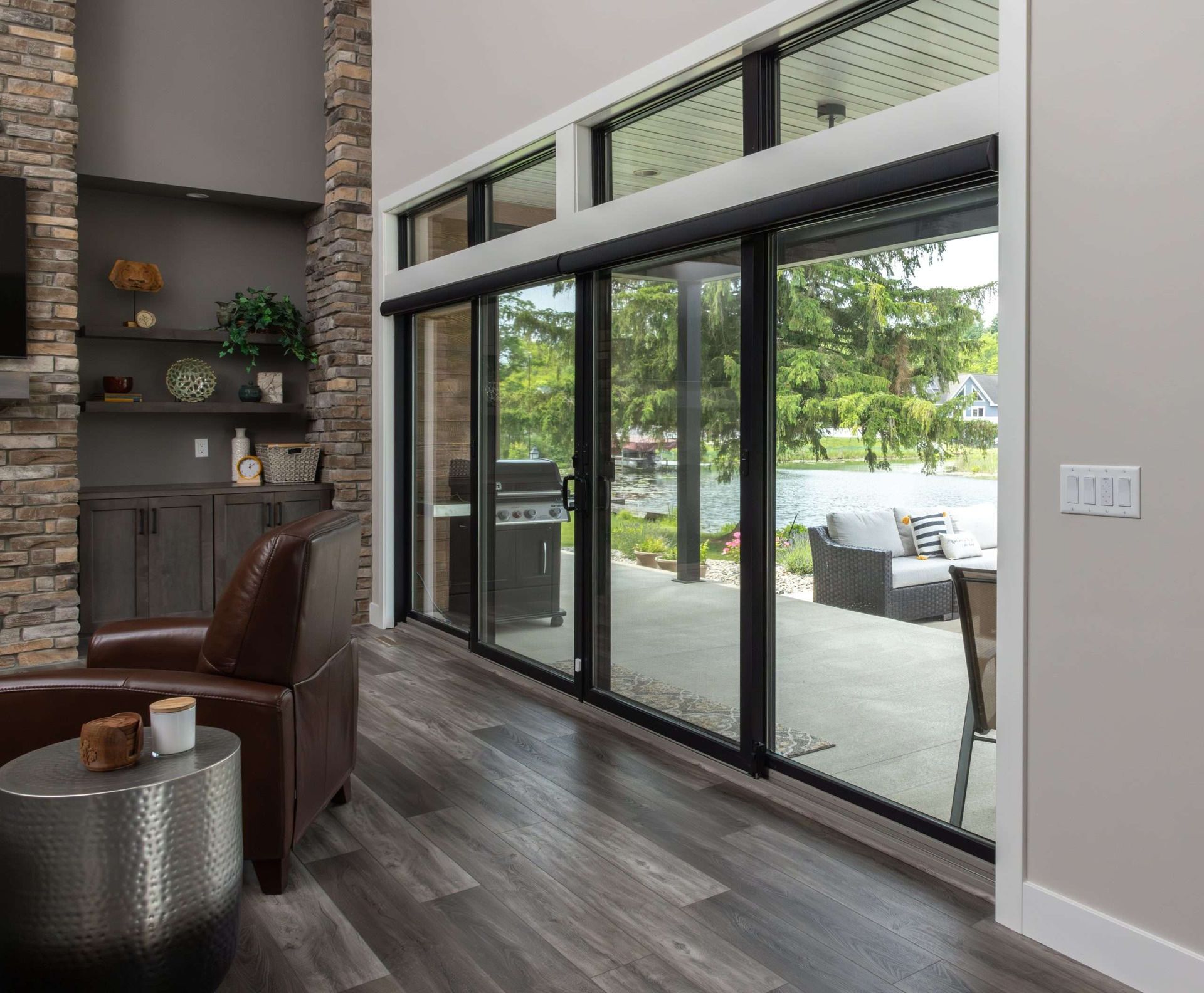 Modern living room with dark wood floors, leather chair, shelving, and large glass sliding doors to a patio.