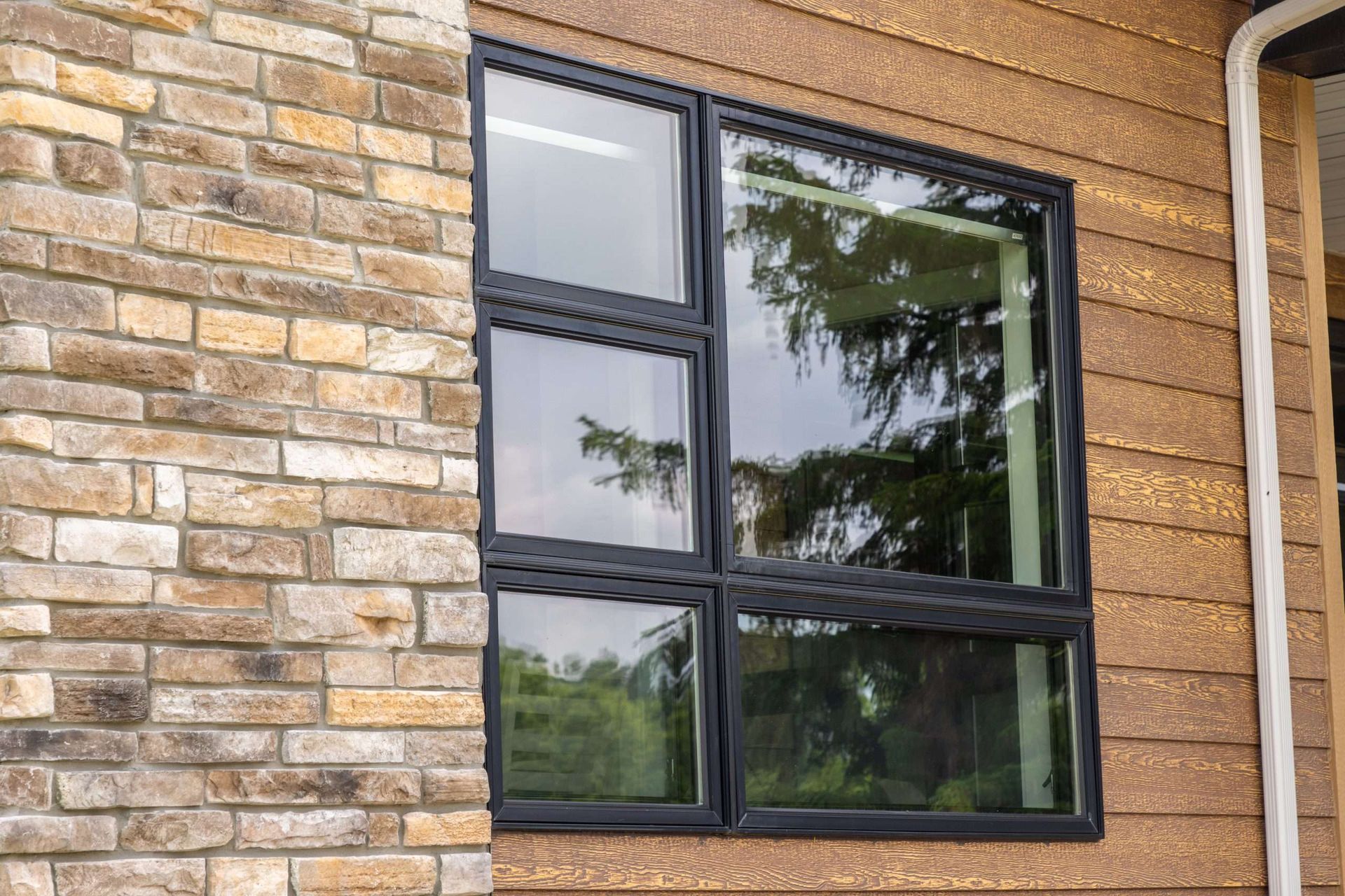 Black-framed window set in a tan brick wall with reflections of trees and sky