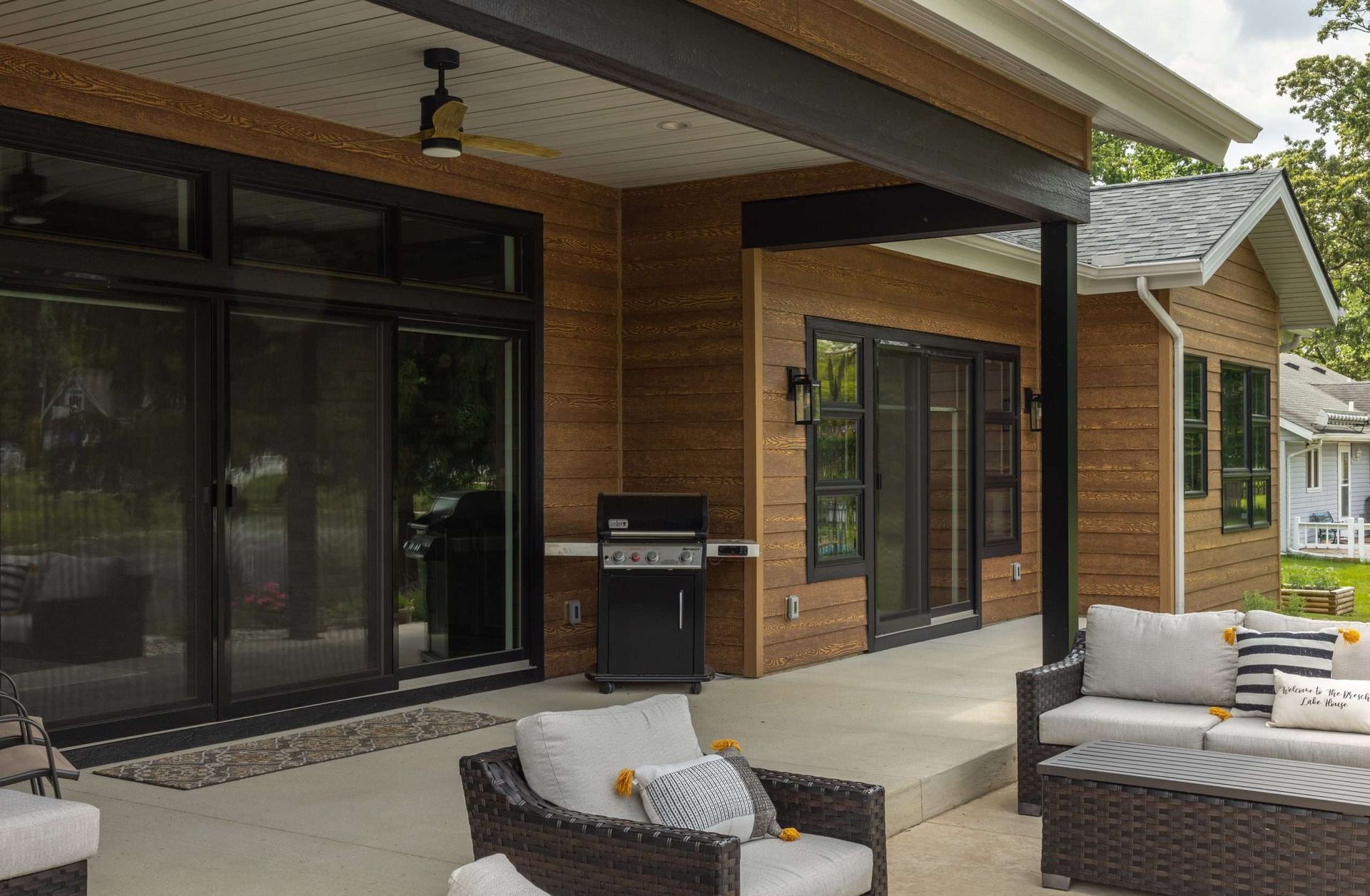 Covered patio with wicker seating, a grill, and sliding glass doors on a brick house