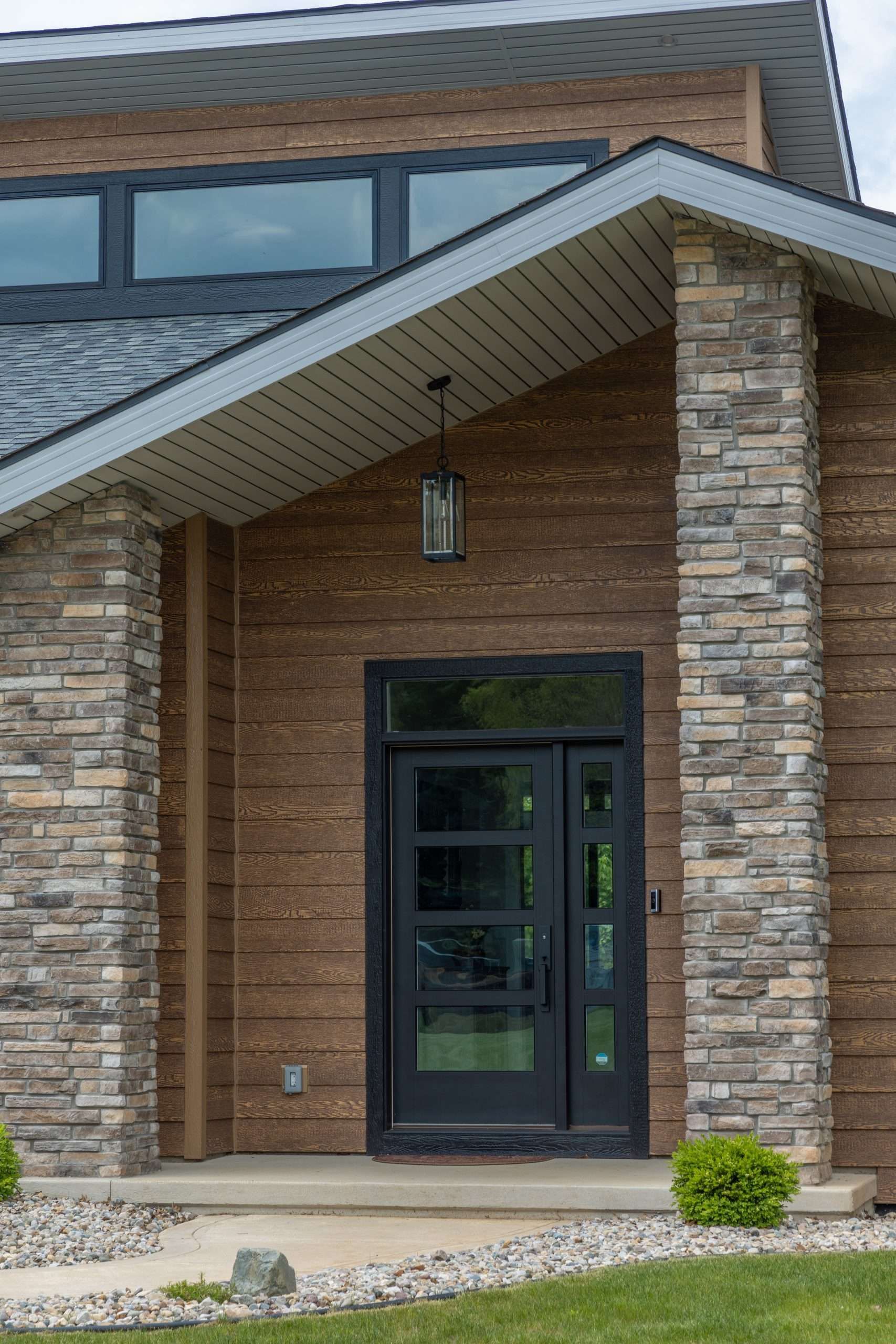 Front entrance of a brick house with a dark door, stone columns, and a sloped porch roof.