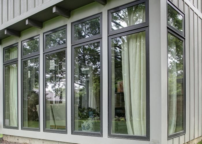 Modern house exterior with large white-framed windows and curtains, reflecting trees outside