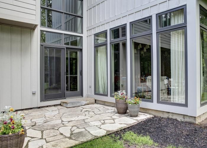 Modern house patio with stone pavers, large windows, and potted plants beside a sliding glass door