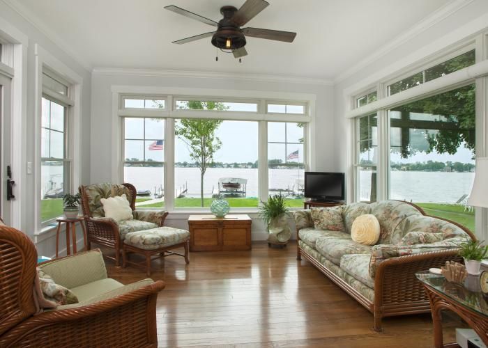 Bright sunroom with wicker seating, hardwood floors, and large windows overlooking a lake.