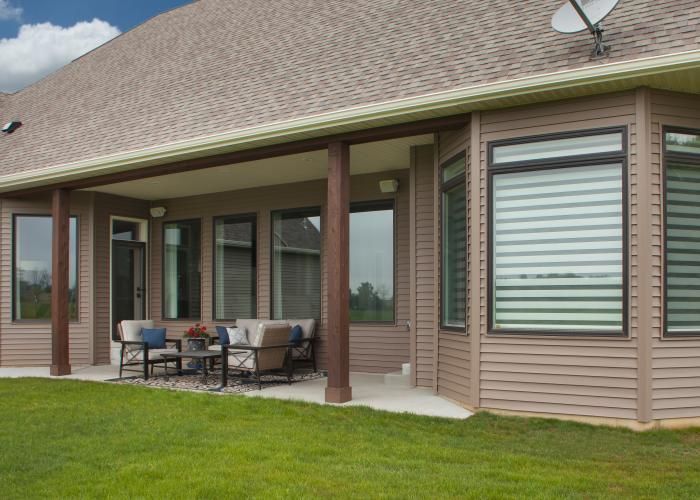 Covered patio with outdoor dining set beside a tan house and green lawn