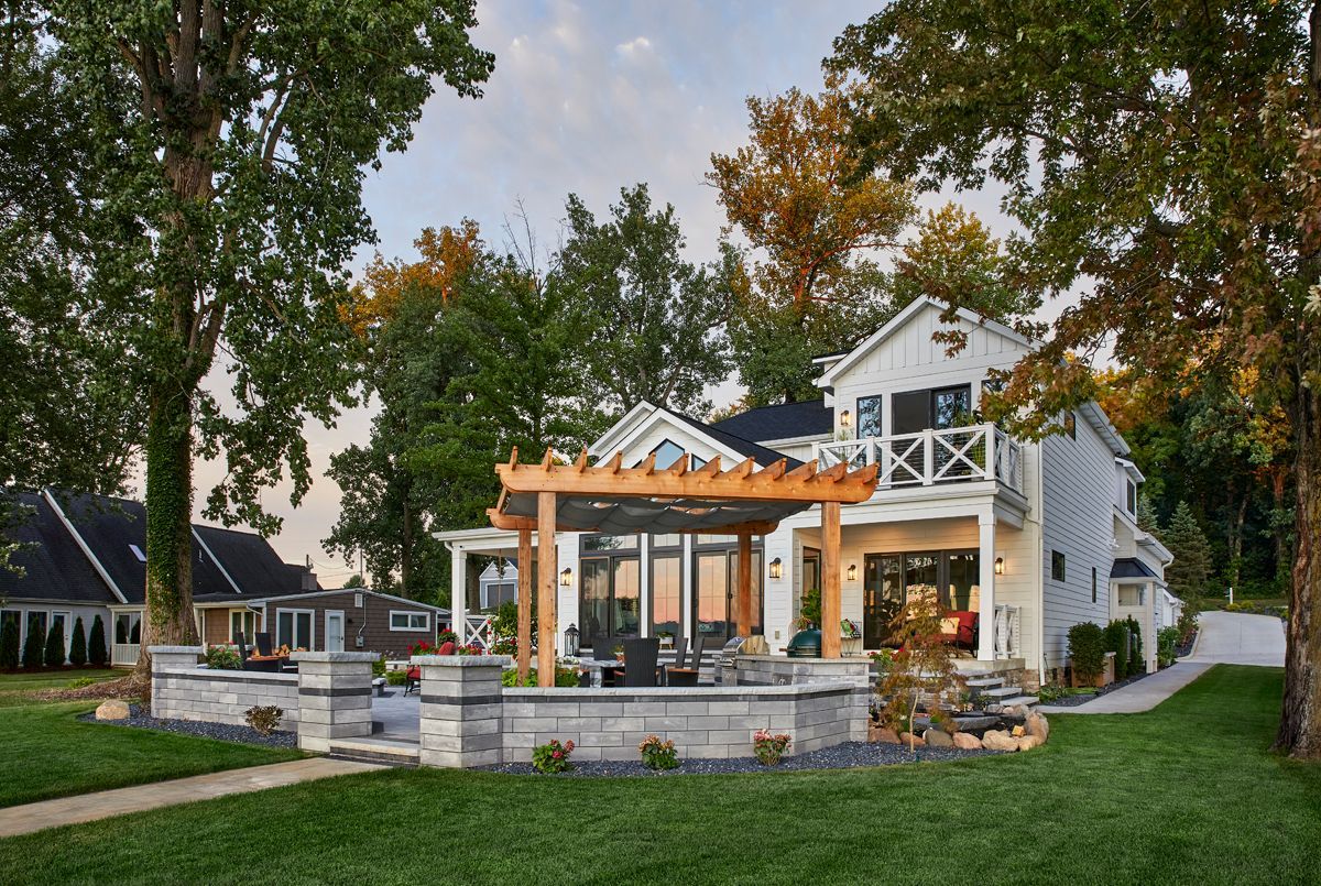 Backyard patio with pergola, stone fire pit, and white house surrounded by trees and grass