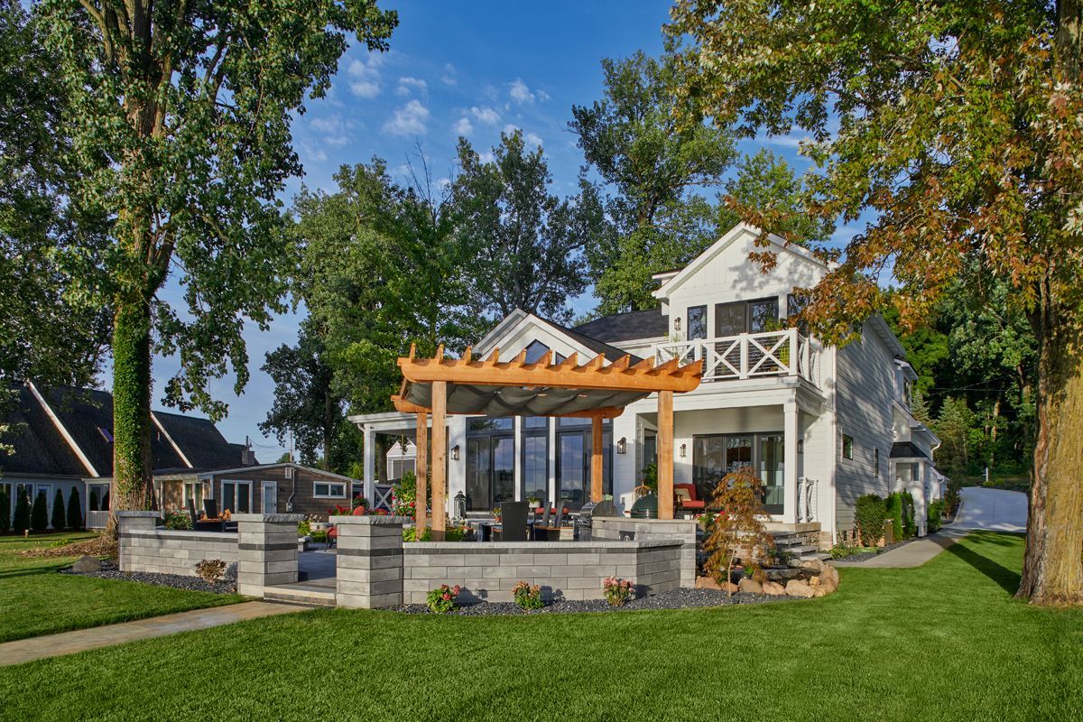 Modern house with a wooden pergola and stone patio beside a green lawn under a blue sky