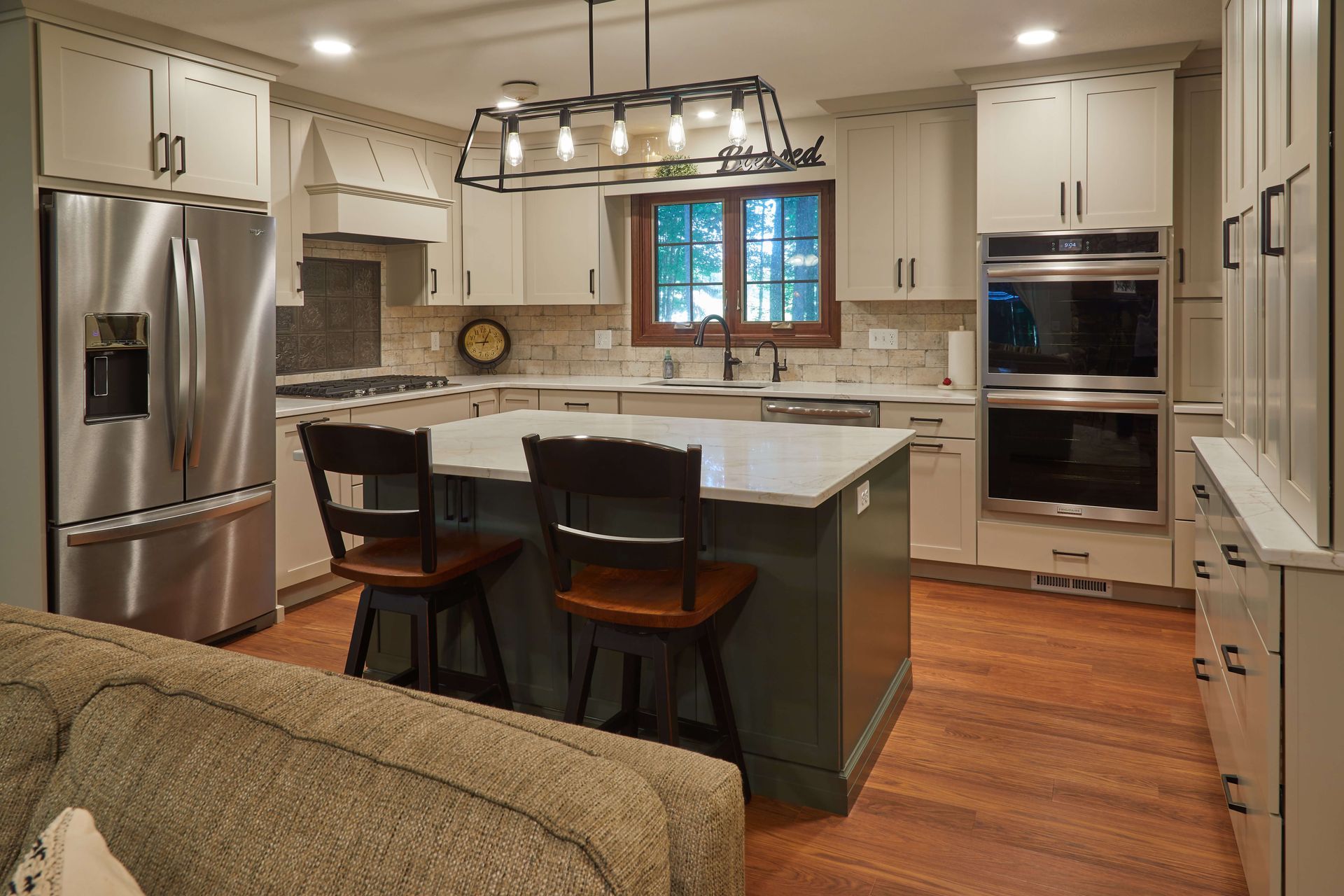 Modern kitchen with white cabinets, stainless appliances, island seating, and warm wood floors