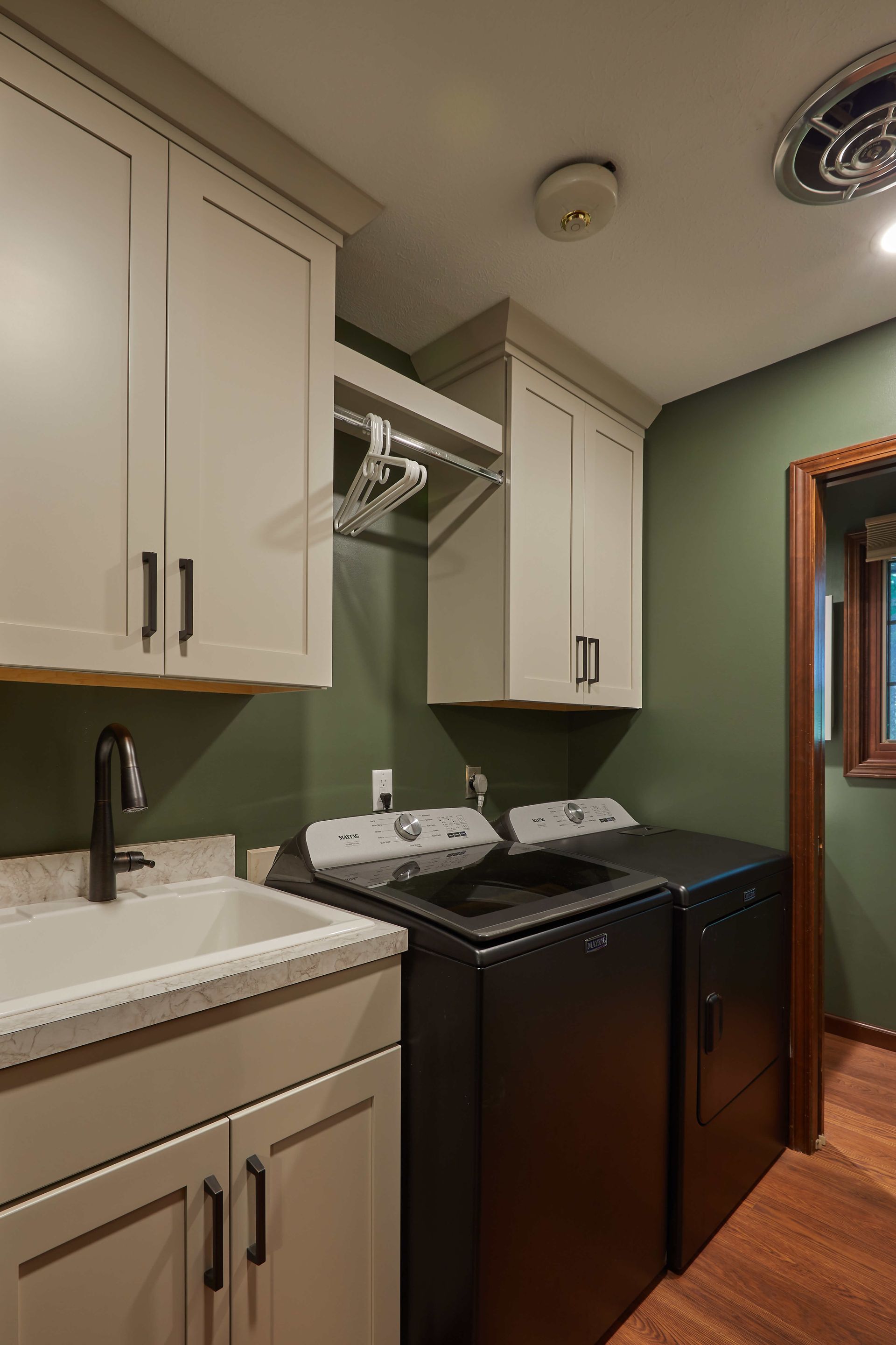 Small laundry room with white cabinets, green walls, black washer and dryer, and a utility sink.