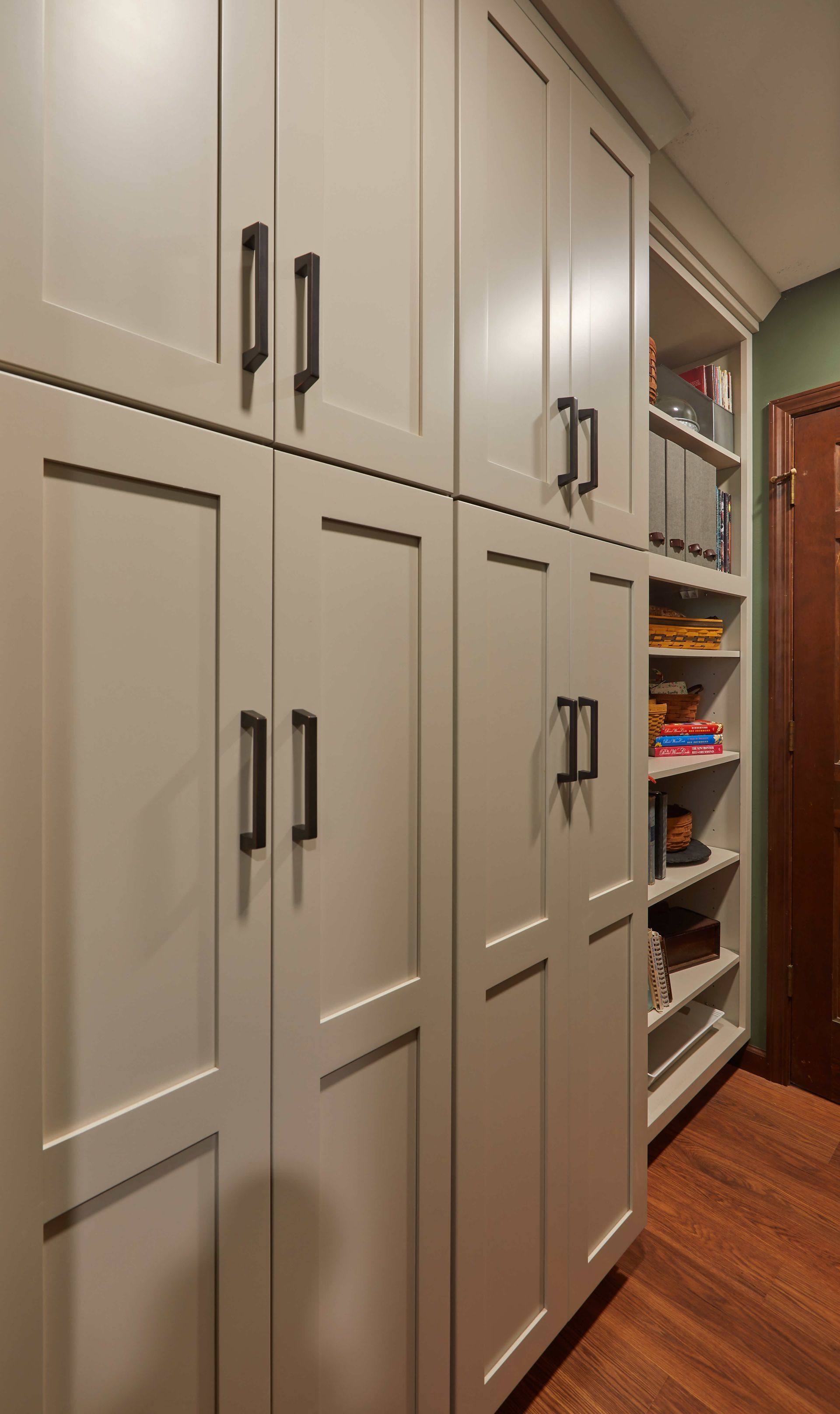 Built-in beige kitchen pantry cabinets beside an open pantry shelf with food items and hardwood floor.