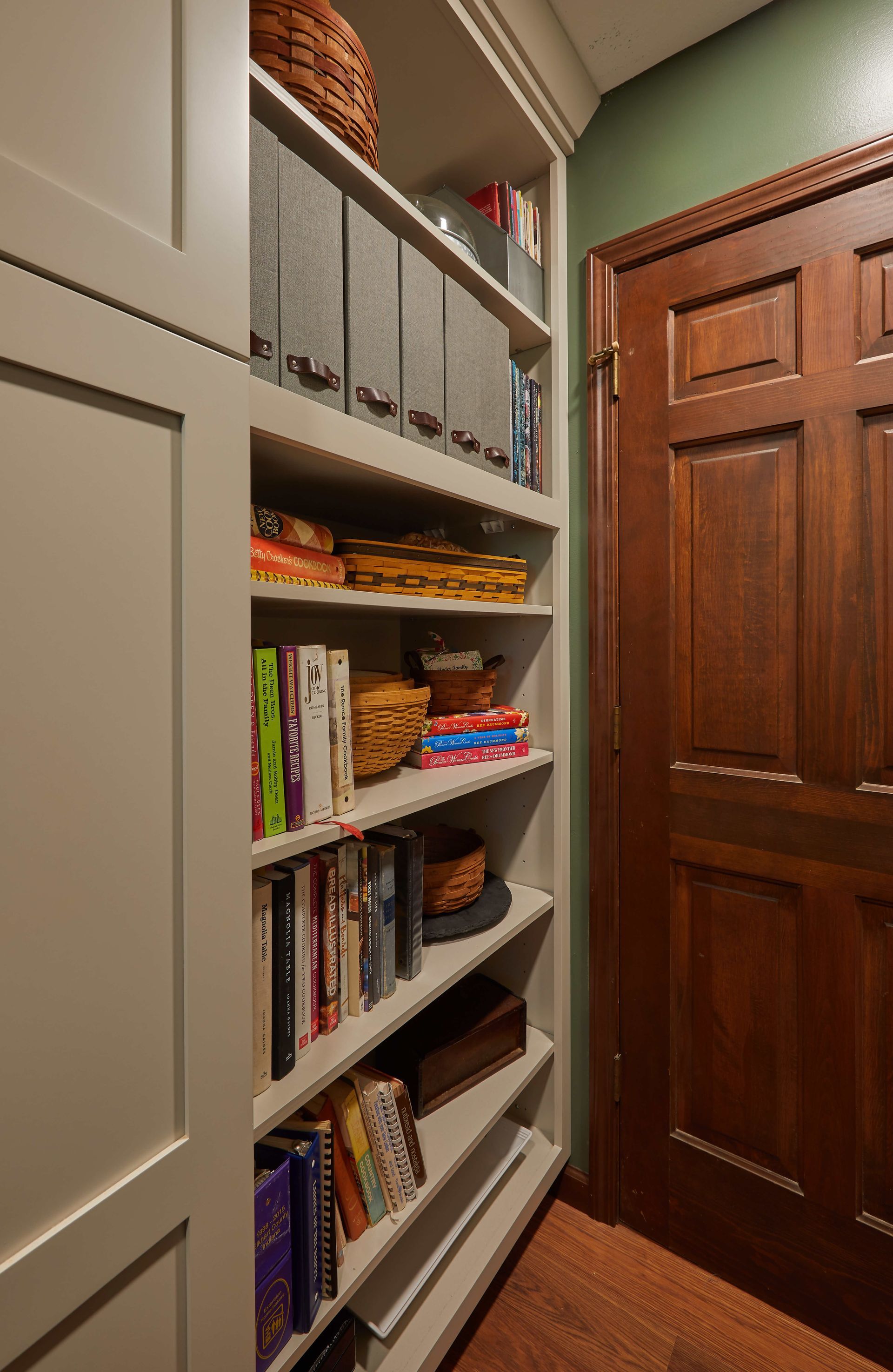 Narrow hallway with built-in shelves filled with books and storage boxes beside a wooden door.