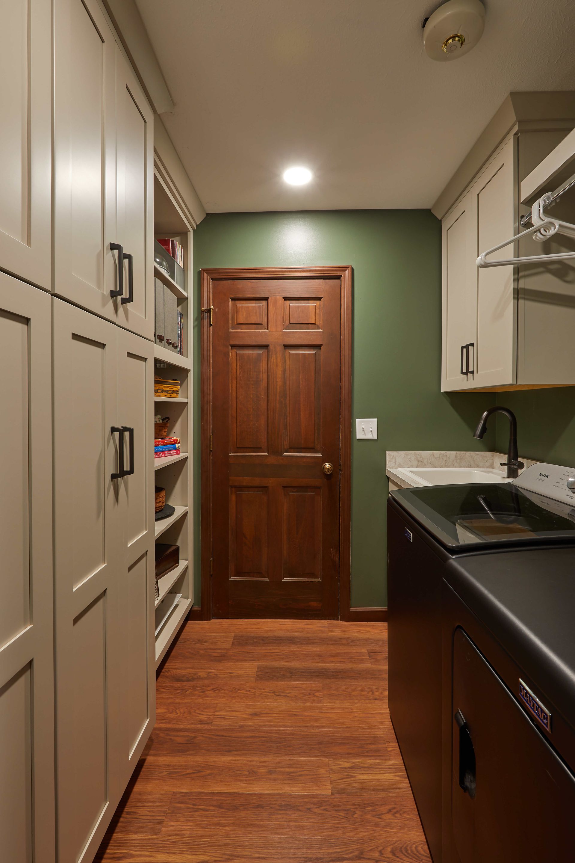 Narrow kitchen hallway with wood door, white cabinets, dark counters, and warm wood floor