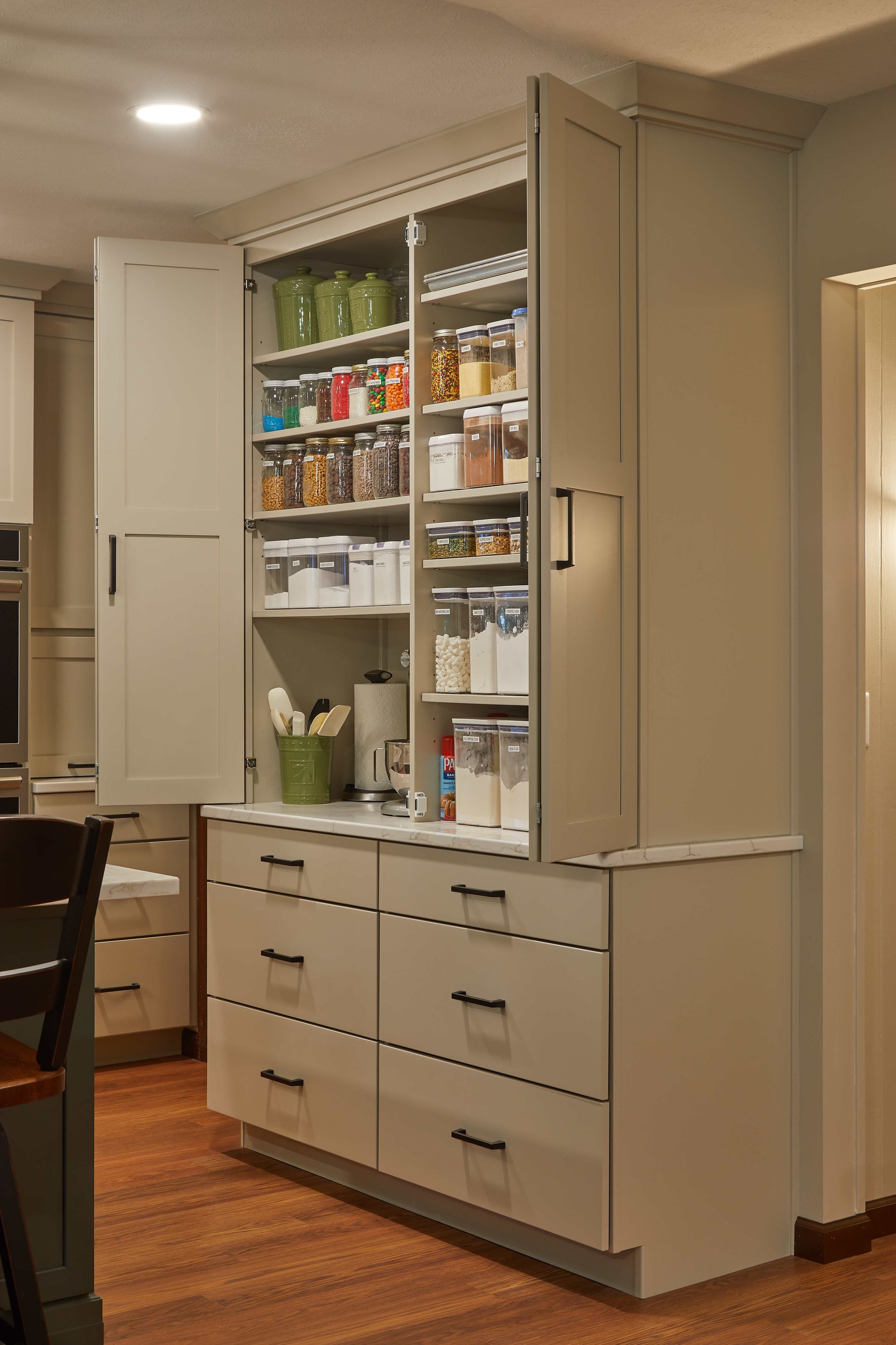 Kitchen pantry cabinet with open shelves, drawers, and organized food containers in a beige room