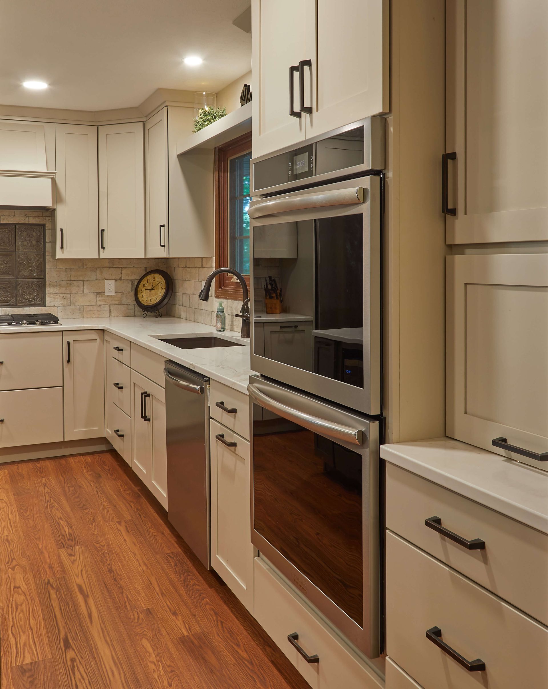 Modern kitchen with white cabinets, stainless built-in oven, wood floor, and granite countertops.