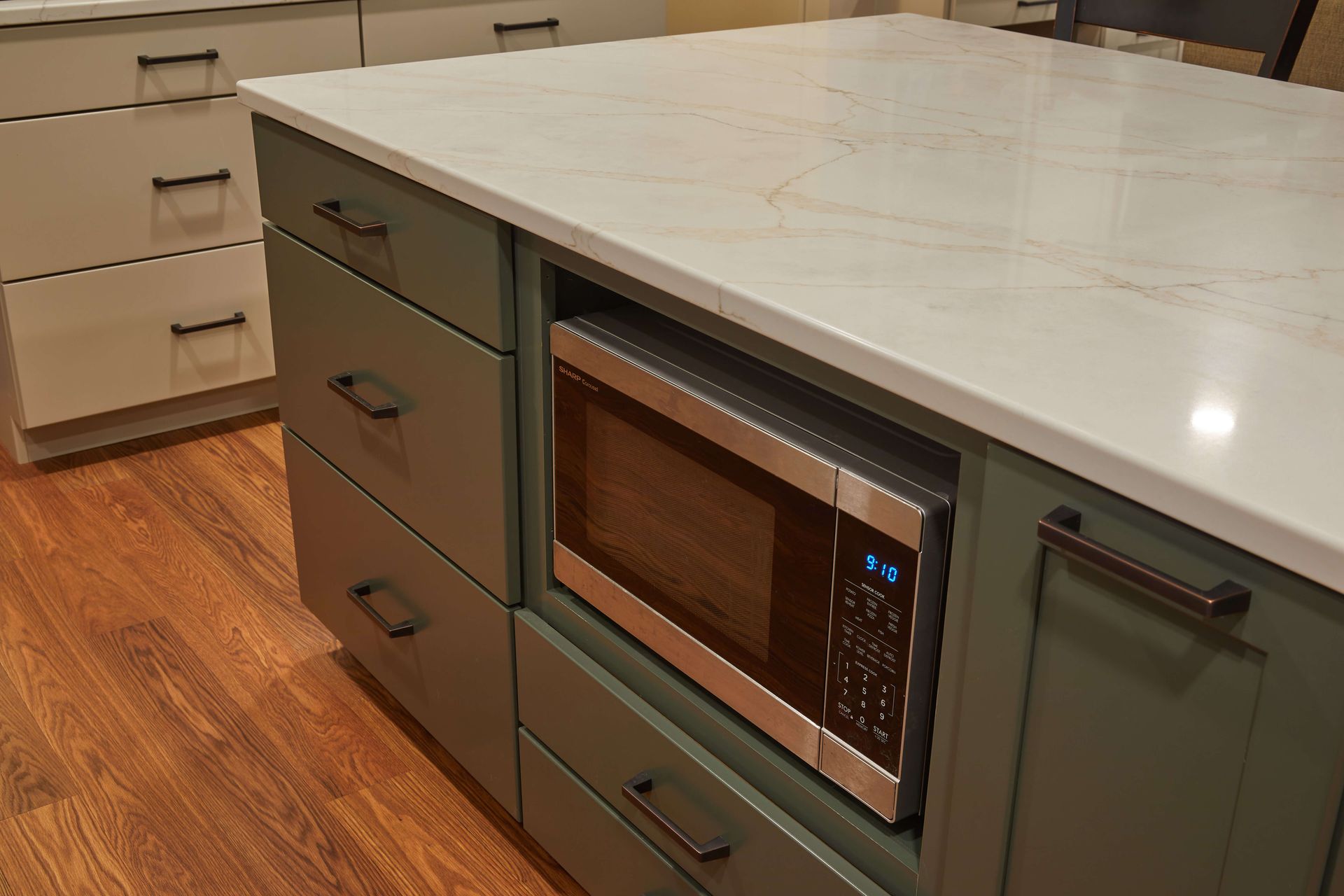 Kitchen island with gray cabinets, white countertop, and built-in microwave in a hardwood-floored kitchen