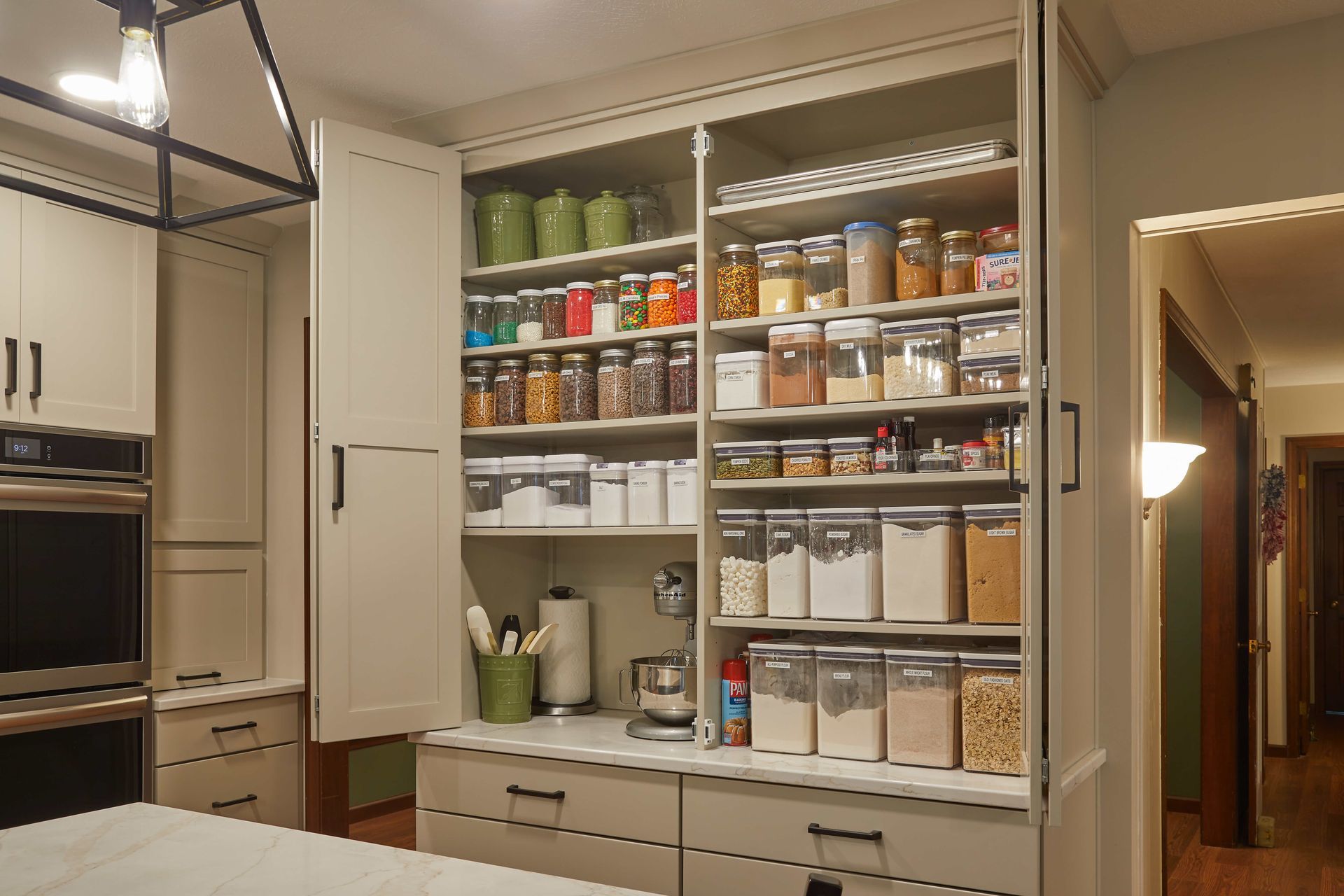 Kitchen pantry cabinet with organized shelves of jars, cans, and containers, and a coffee maker below