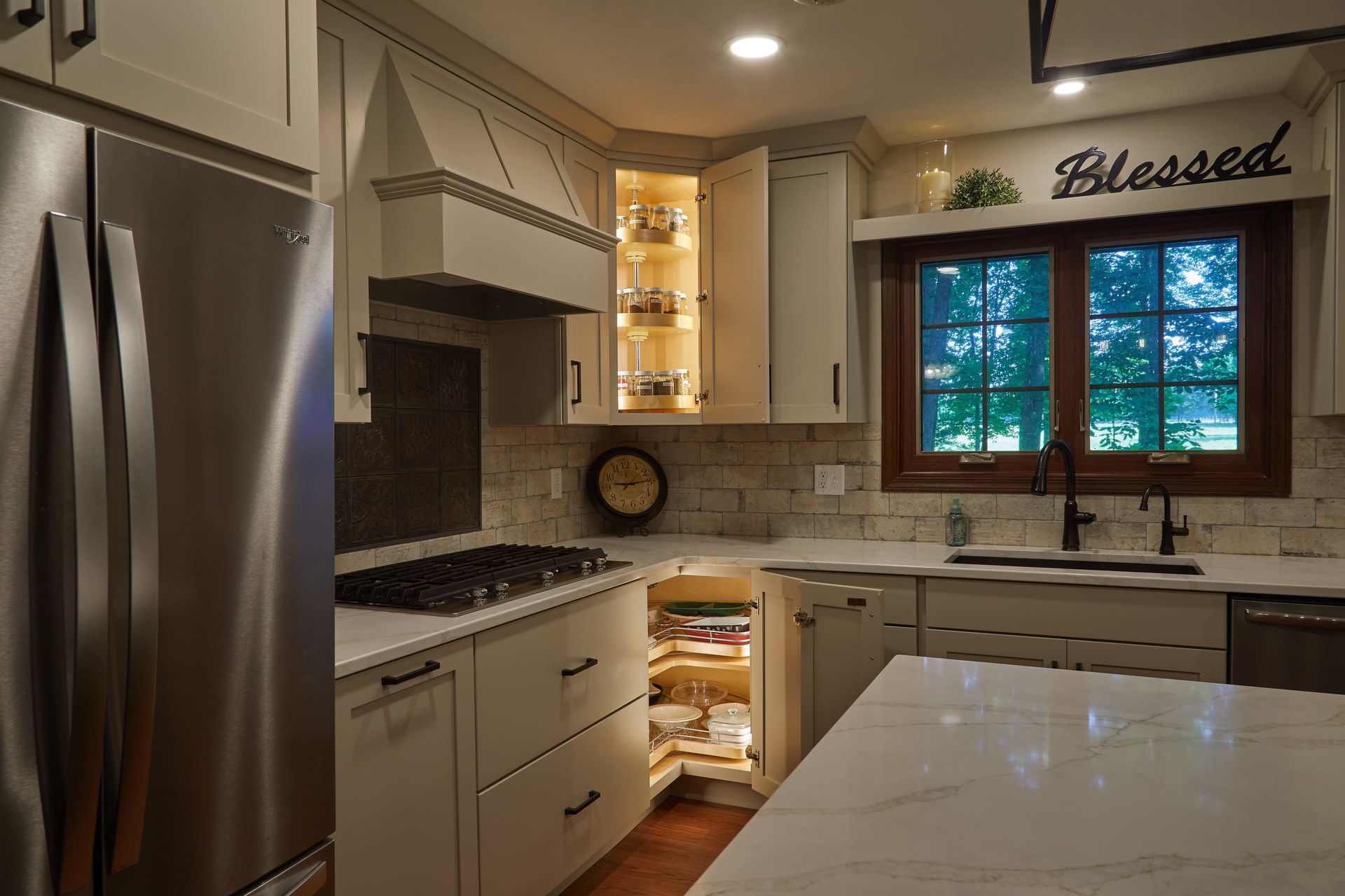 Bright kitchen with stainless fridge, white cabinets, marble island, and a window above the sink
