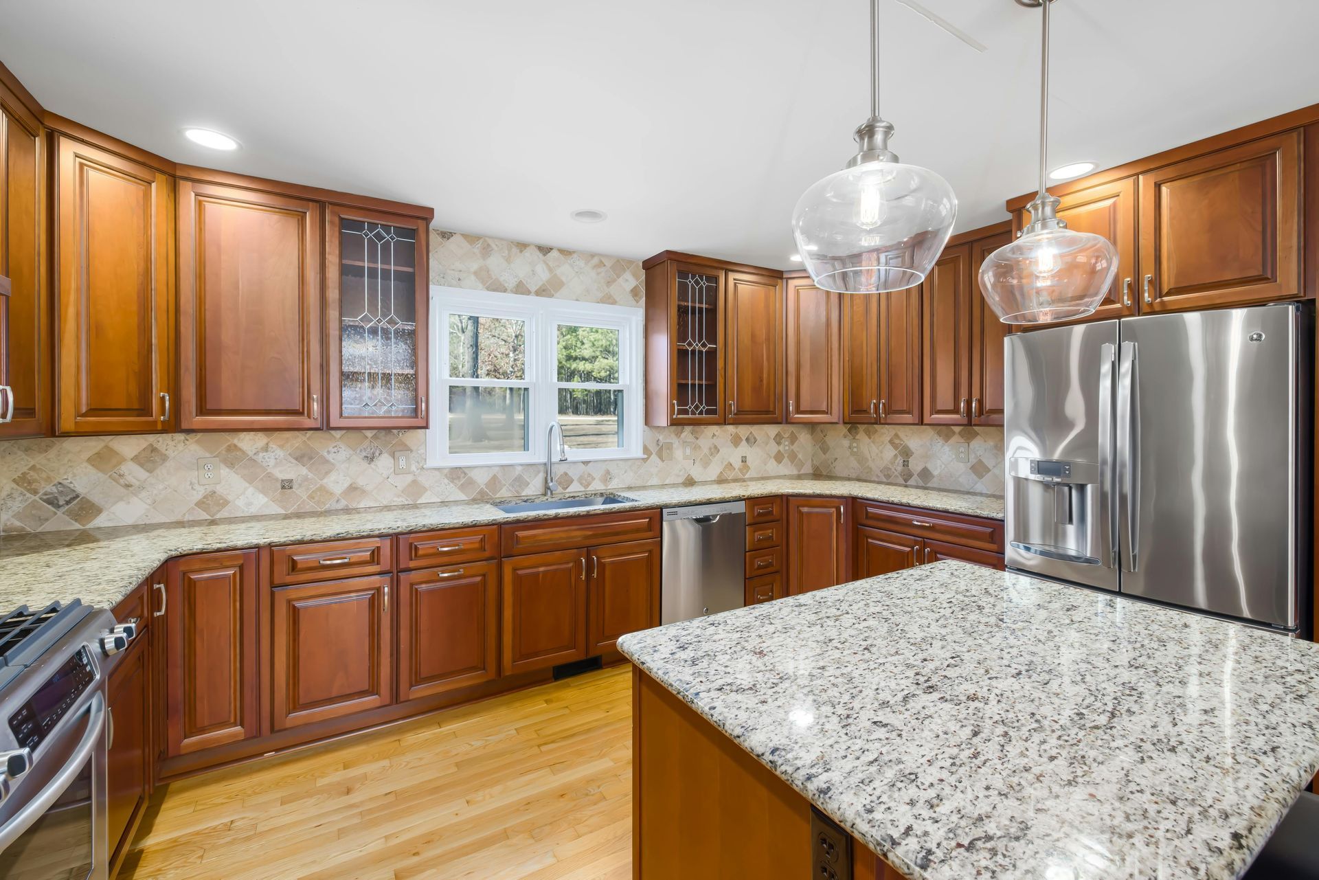 Bright kitchen with wood cabinets, granite island, stainless fridge, and pendant lights