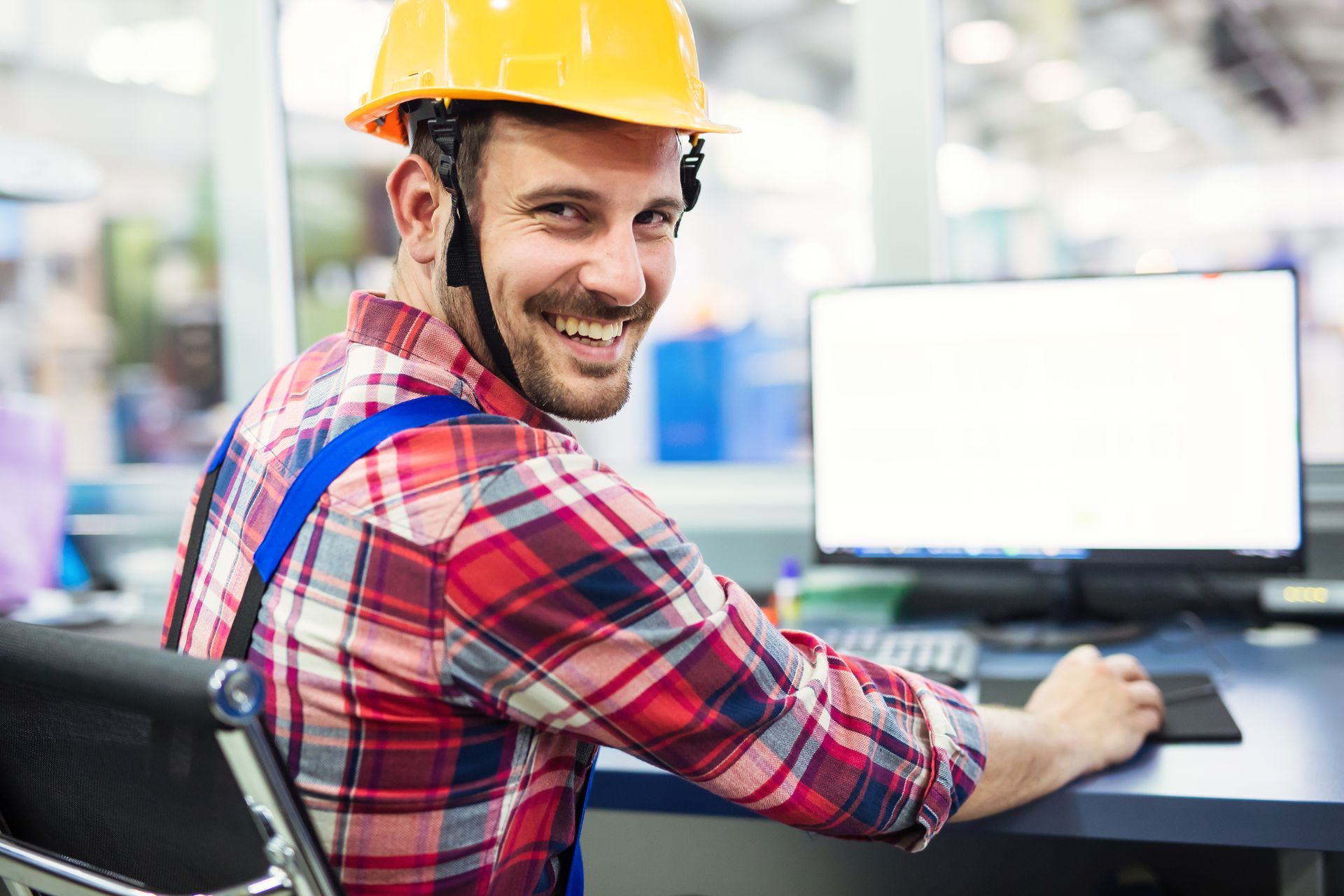 A man wearing a hard hat is sitting at a desk in front of a computer.