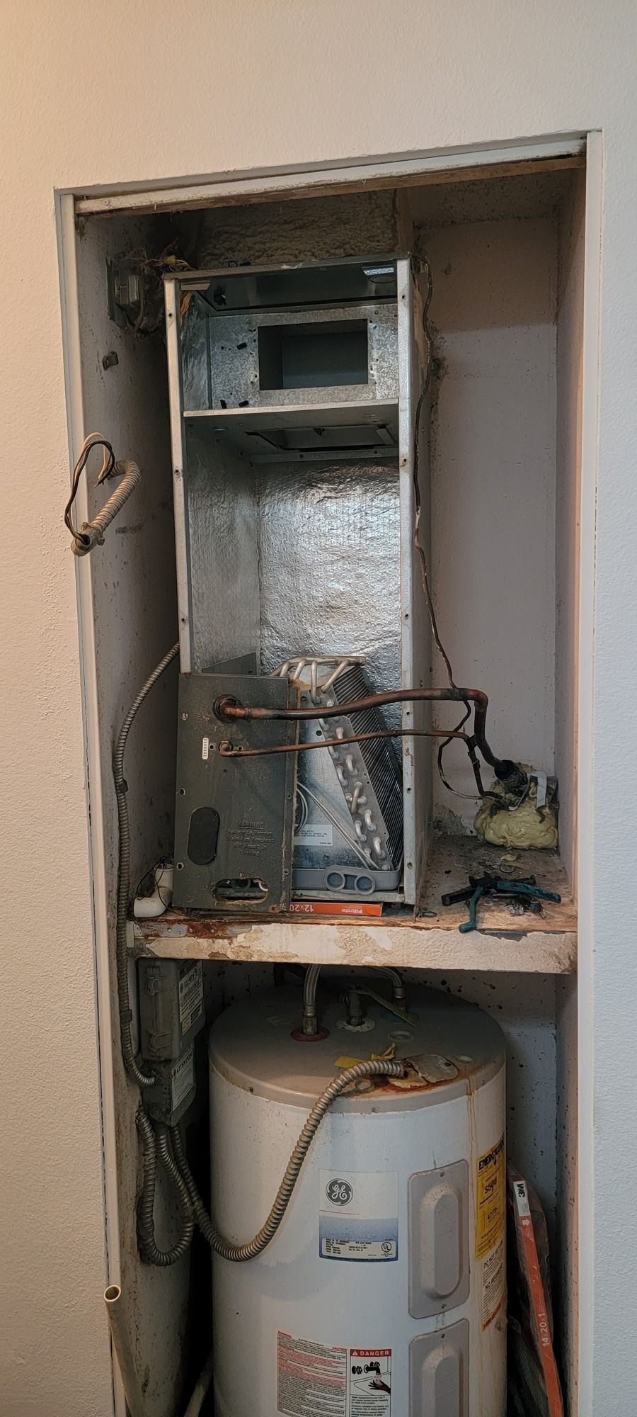 A water heater is sitting on top of a shelf in a closet.