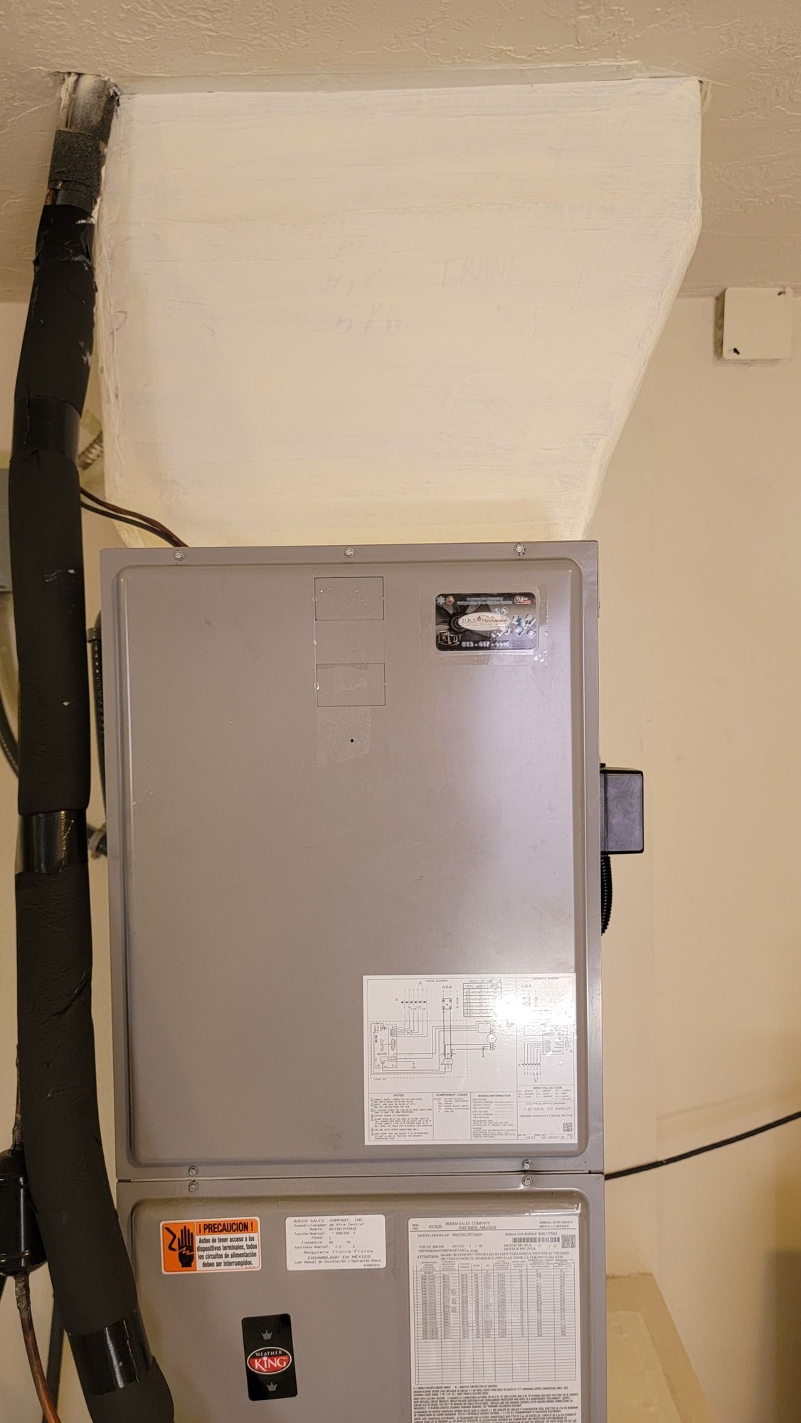 A gray air conditioner is sitting on top of a white wall in a room.