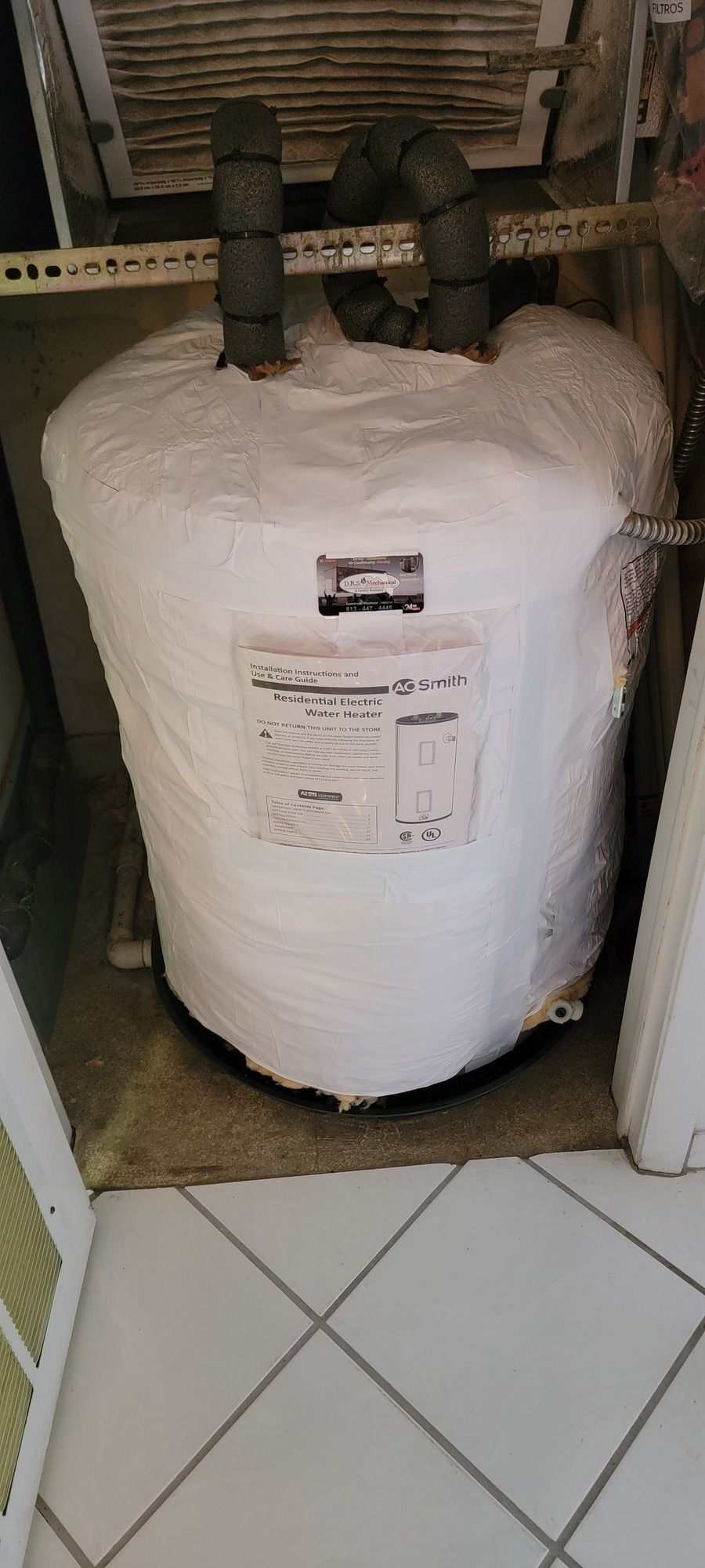 A large white water heater is sitting on a tiled floor next to a door.