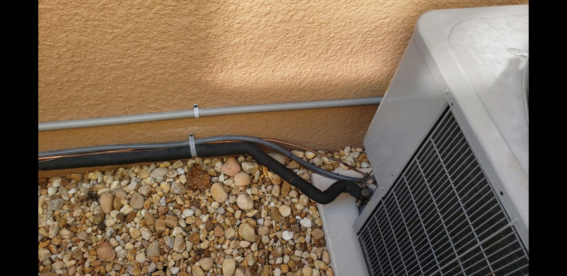 An air conditioner is sitting on a pile of rocks next to a wall.