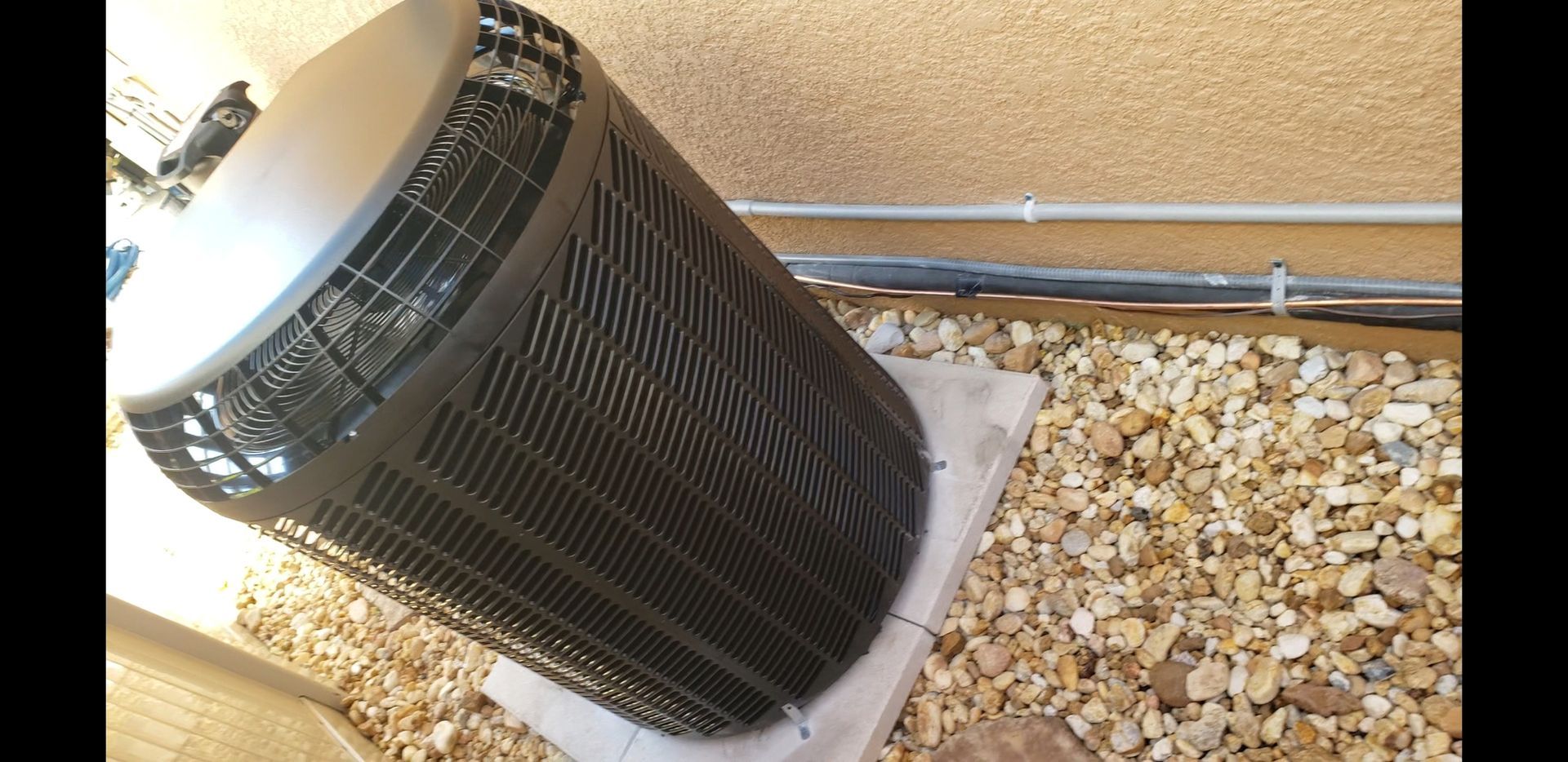 A black air conditioner is sitting on a pile of rocks.