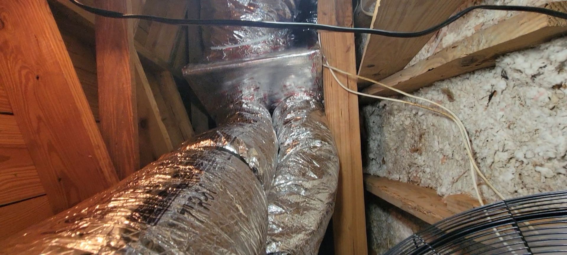 A fan is sitting next to a duct in an attic.