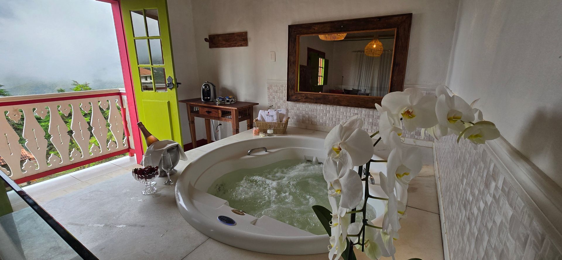 Banheira de hidromassagem na varanda com orquídeas, espelho e porta aberta com vista para o mar.