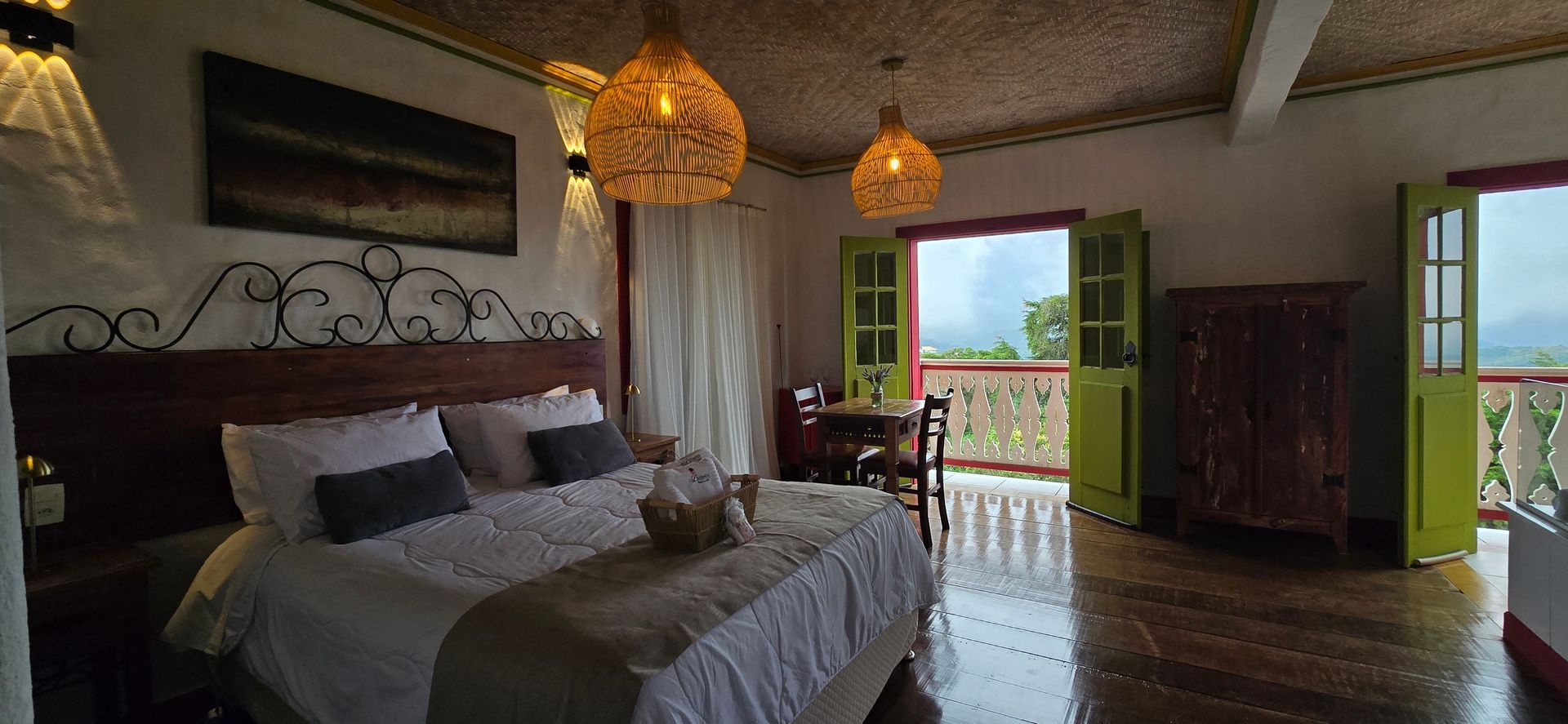 Quarto aconchegante com cama, luminárias pendentes e portas abertas para uma varanda com vista para o mar.