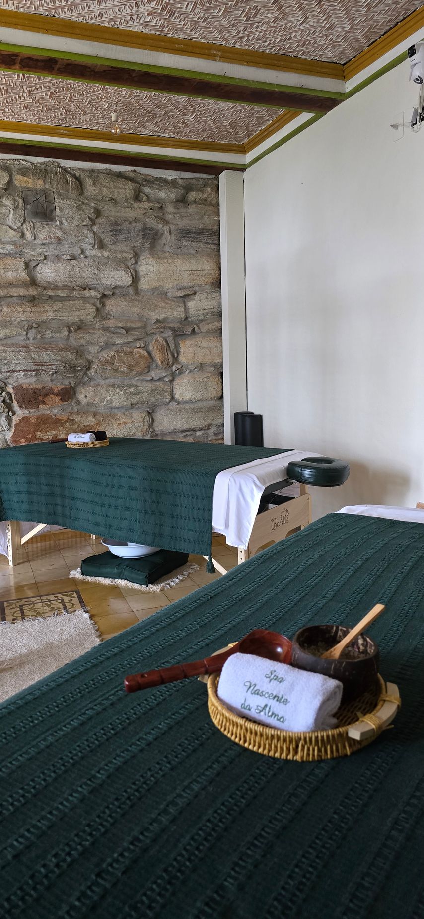 Sala de jantar rústica com parede de pedra, toalhas de mesa verdes e uma cesta de vime sobre a mesa.