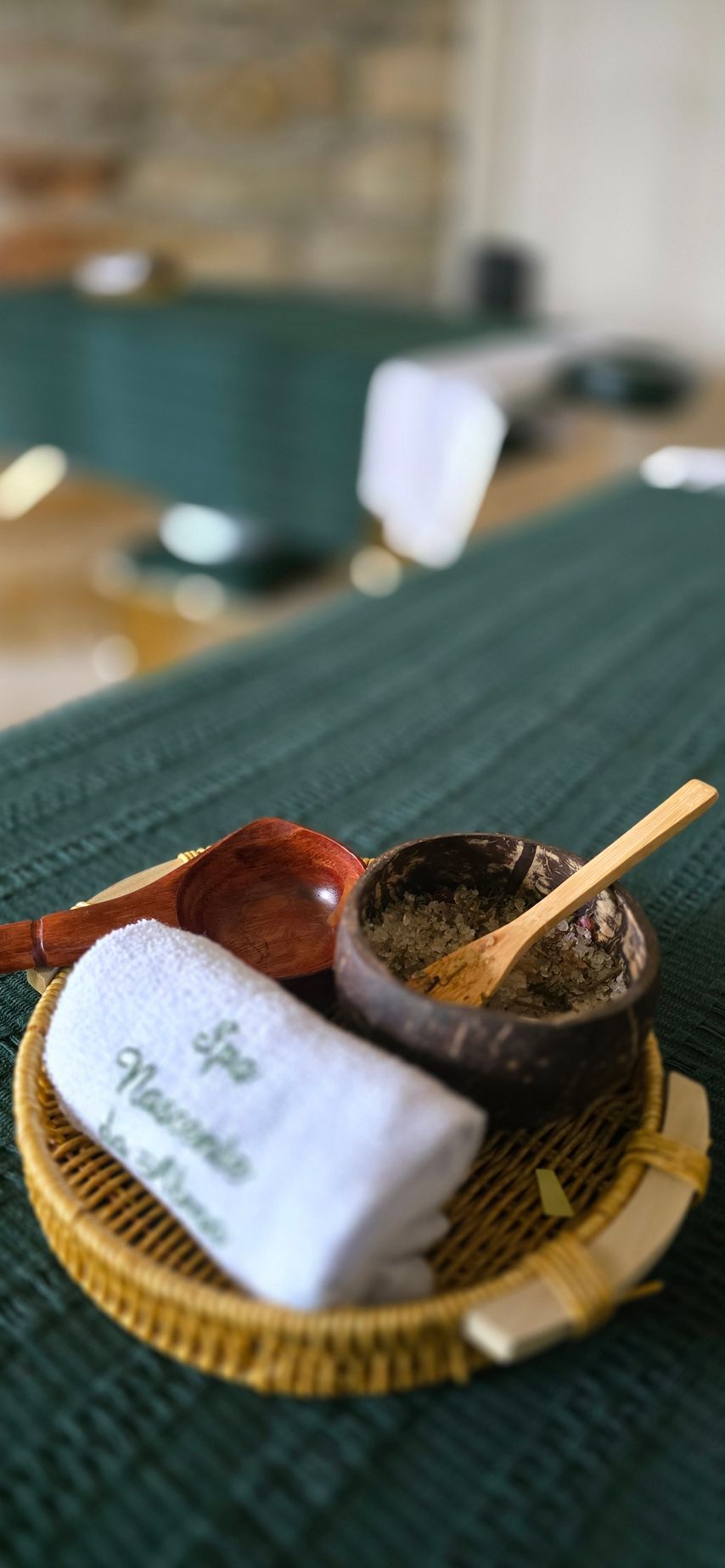 Bandeja de vime com xícaras e colher sobre uma toalha de mesa verde em um café com desfoque suave.