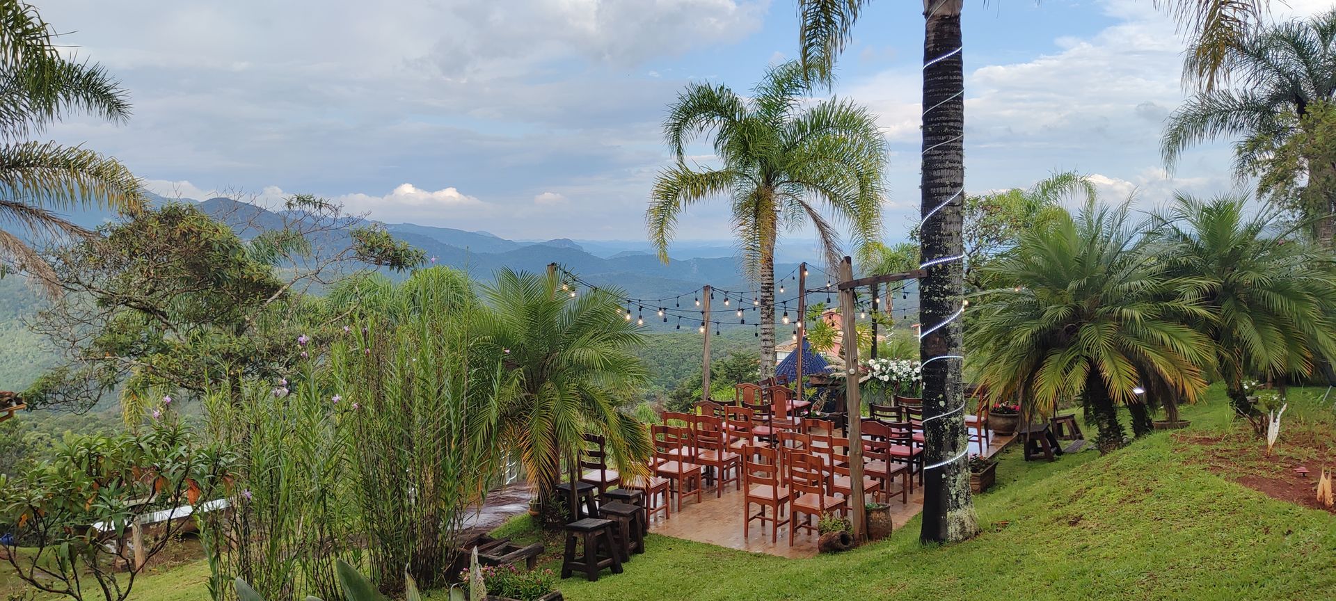 Resort tropical na encosta de uma colina com palmeiras, deck de madeira e vista para a montanha sob um céu nublado.