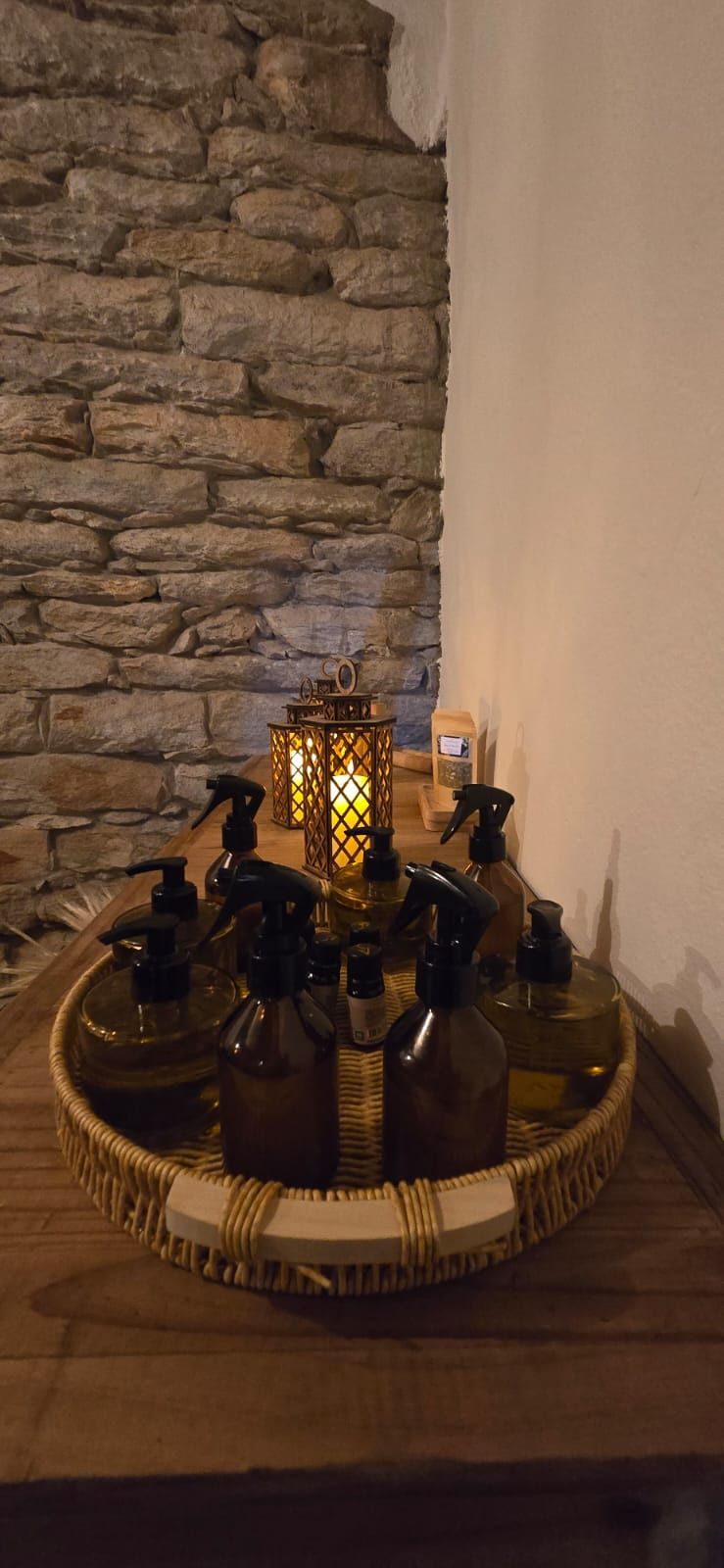 Arranjo decorativo de mesa com velas acesas, flores e detalhes dourados ao lado de uma parede de pedra.