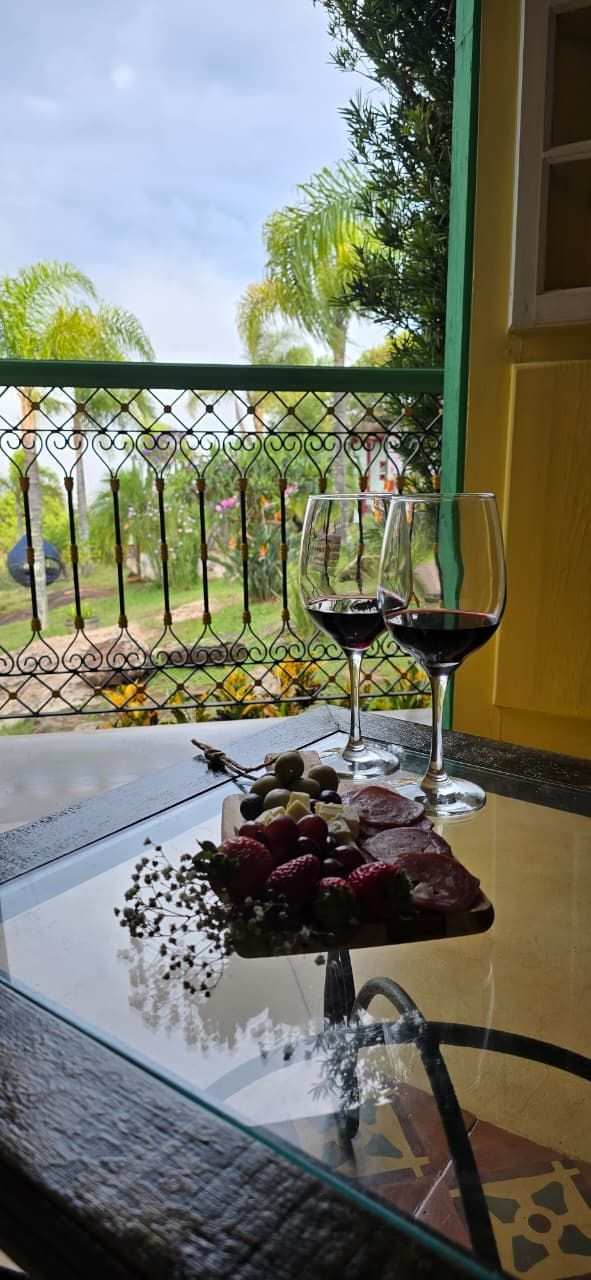 Vista da varanda com taças de vinho e uma fruteira sobre a mesa, com vista para palmeiras e vegetação.