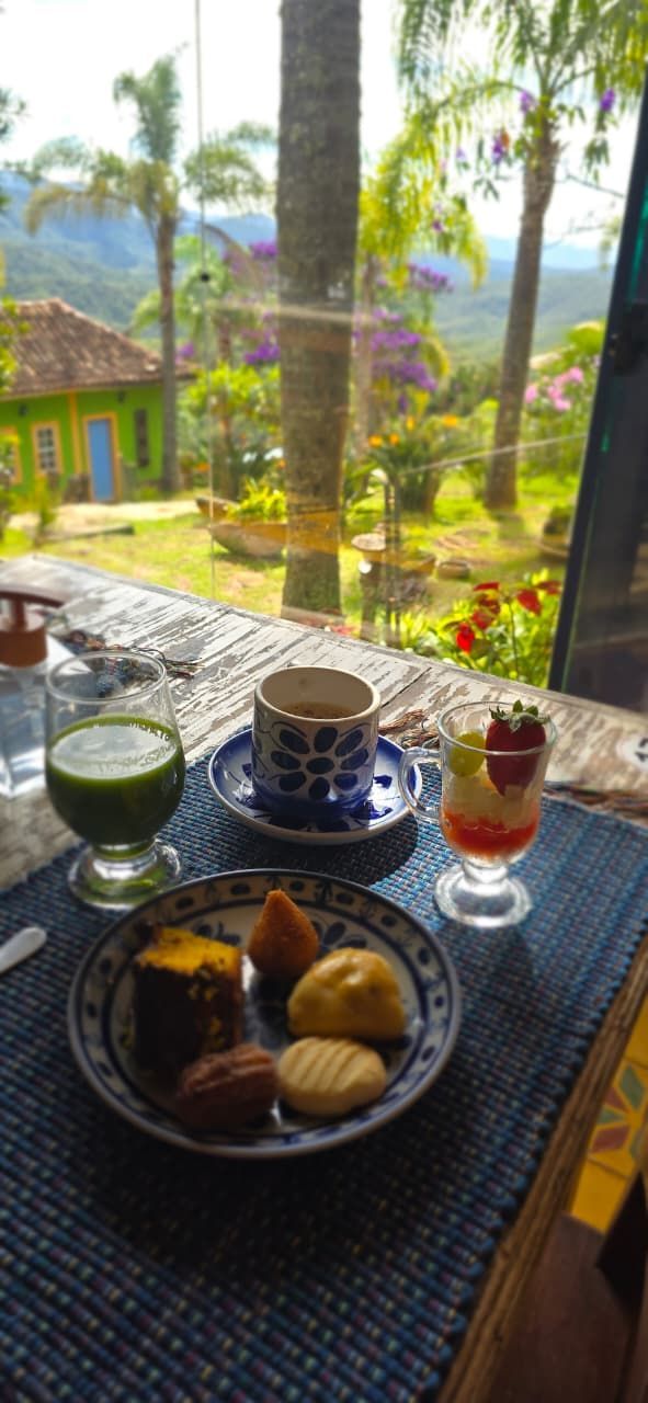 Café da manhã em um terraço com vista para jardins exuberantes, com café, chá e frutas à disposição.