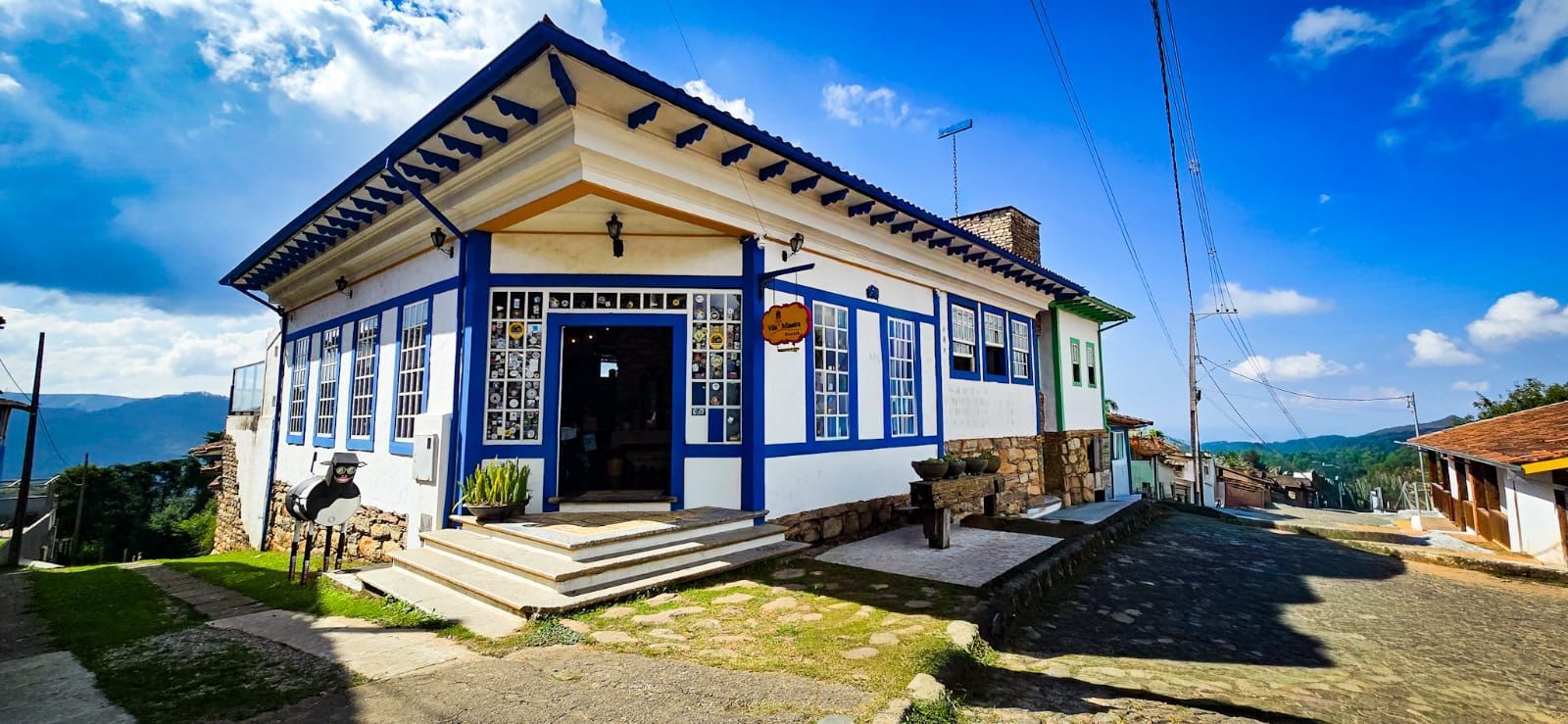 Pequeno prédio branco e azul com telhado em forma de pico numa esquina ensolarada.