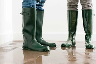 Two people wearing green rubber boots standing in flooded room.