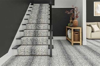 Staircase with patterned runner, dark wall, side table with decor, and light carpet flooring.