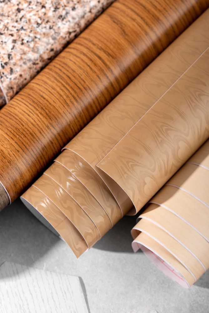 Rolls of patterned adhesive shelf liners: granite, wood grain, and tan wood-look.