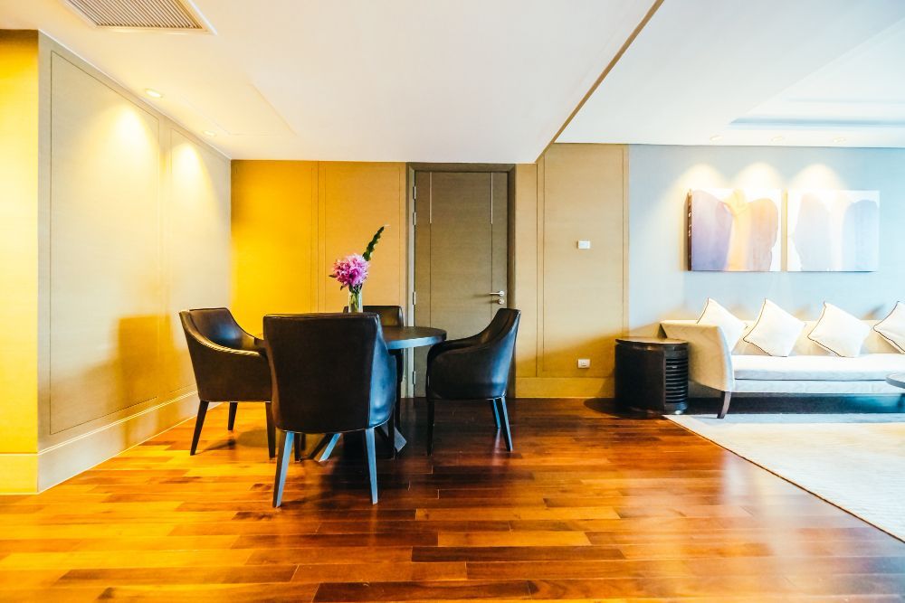 Dining area with round table and four black chairs; hardwood floor, tan walls, and a sofa.