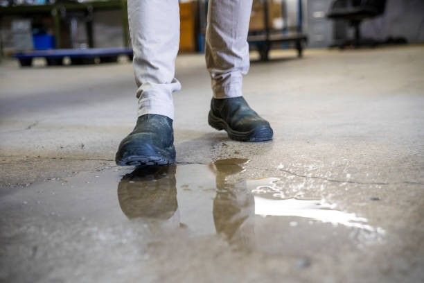 Person in work boots standing in a puddle on a concrete floor, reflective surface.